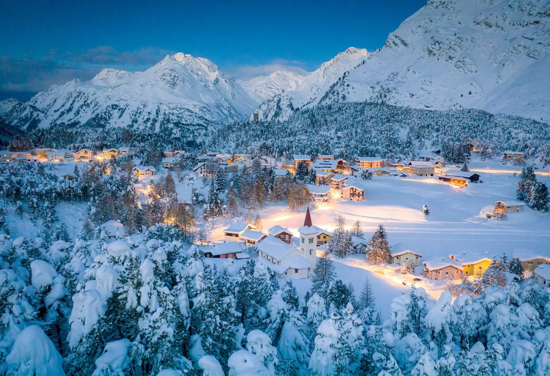 Maloja alpine village and Chiesa Bianca framed by snowy woods at dusk, Bregaglia, canton of Graubunden, Engadin, Switzerland
