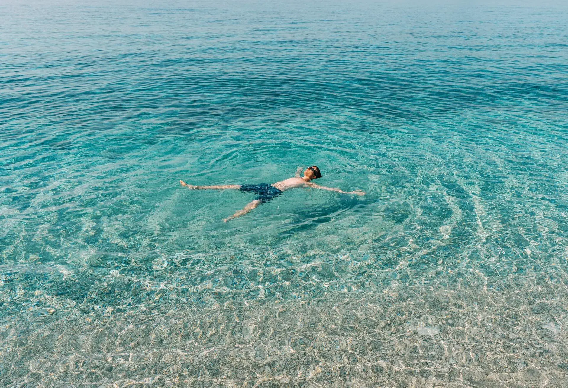 Young man have a fun in turquoise sea. High angle view of man lying like star. 