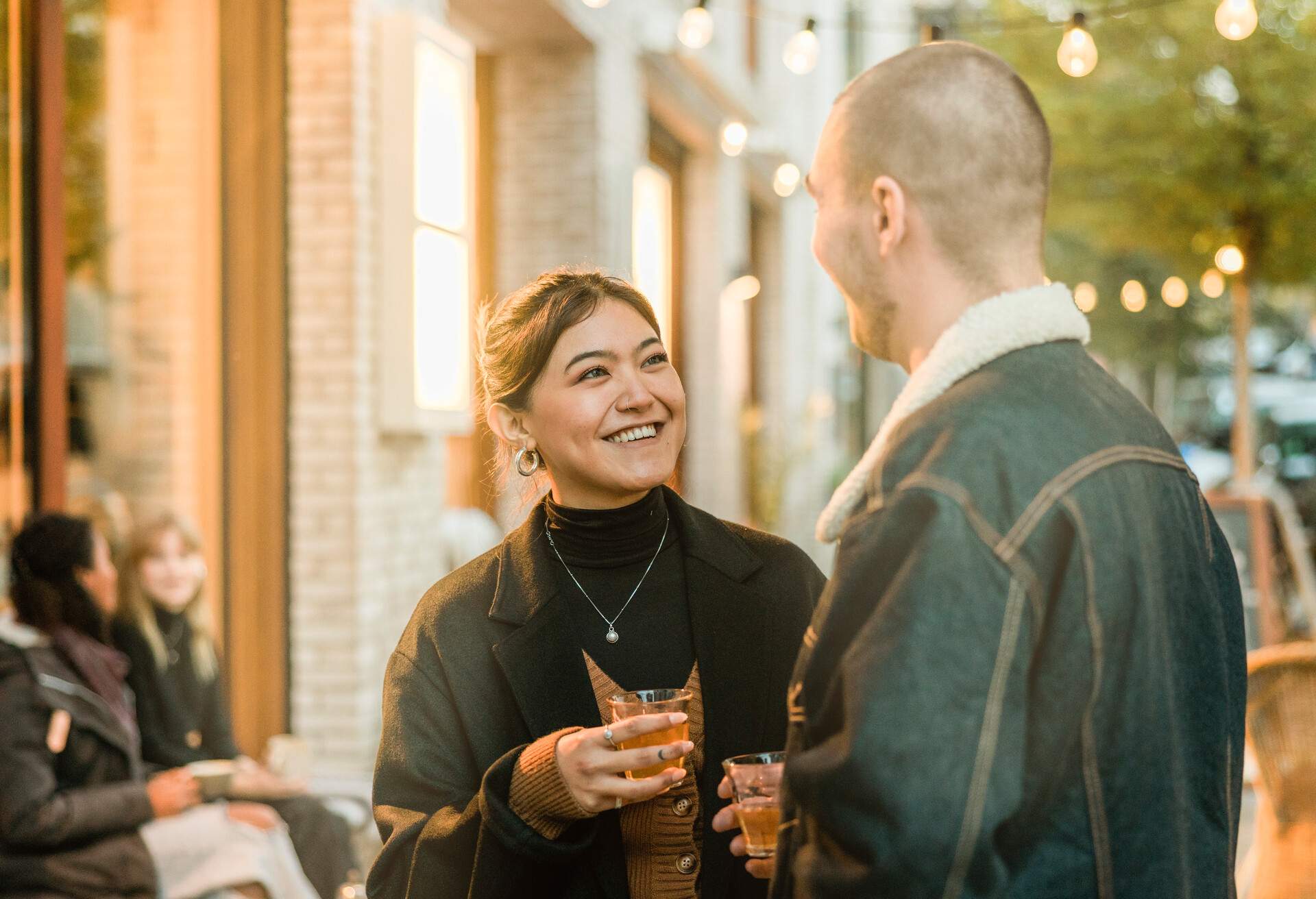 Couple talking over a hot cup of tea on a winter evening outside a cafe in the city. Young woman holding a tea and talking with her boyfriend while standing outside a coffee shop.