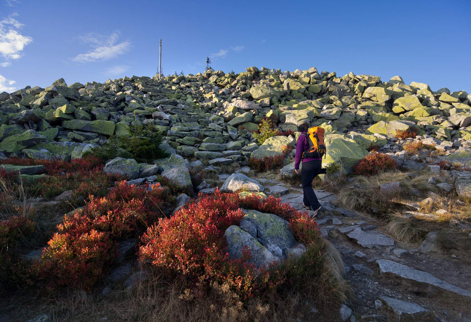 A woman hiking on a rocky trail to the summit of a mountain.