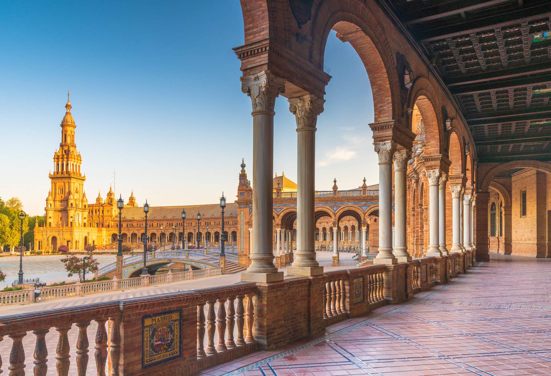 Sunrise on the old tower seen from colonnade of the semi-circular portico, Plaza de Espana, Seville, Andalusia, Spain