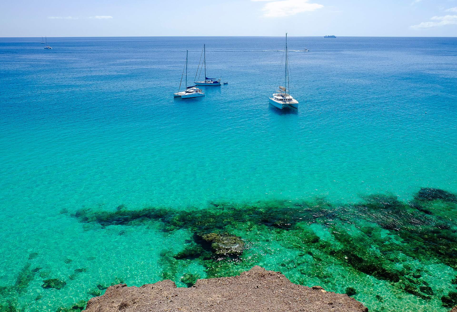 View on the ocean with crystal water and three woutistic boats in Morro Jable on the Canary island Fuerteventura, Spain.