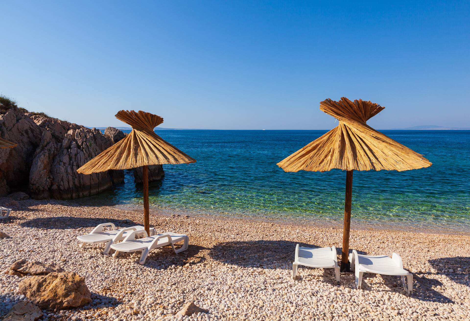 View of the straw umbrellas in the beautiful Oprna beach in the adriatic bay of the Krk island, Croatia