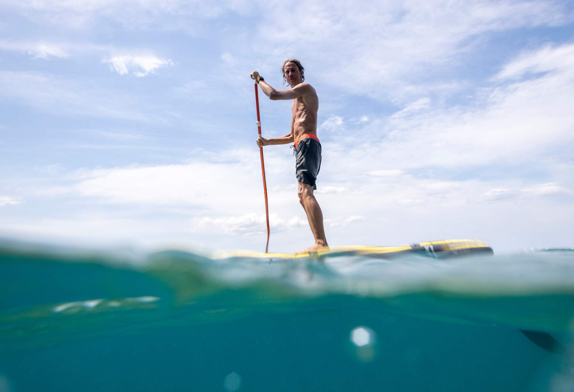 Taken between water and sky, male paddling on SUP board with cristal clear water below.