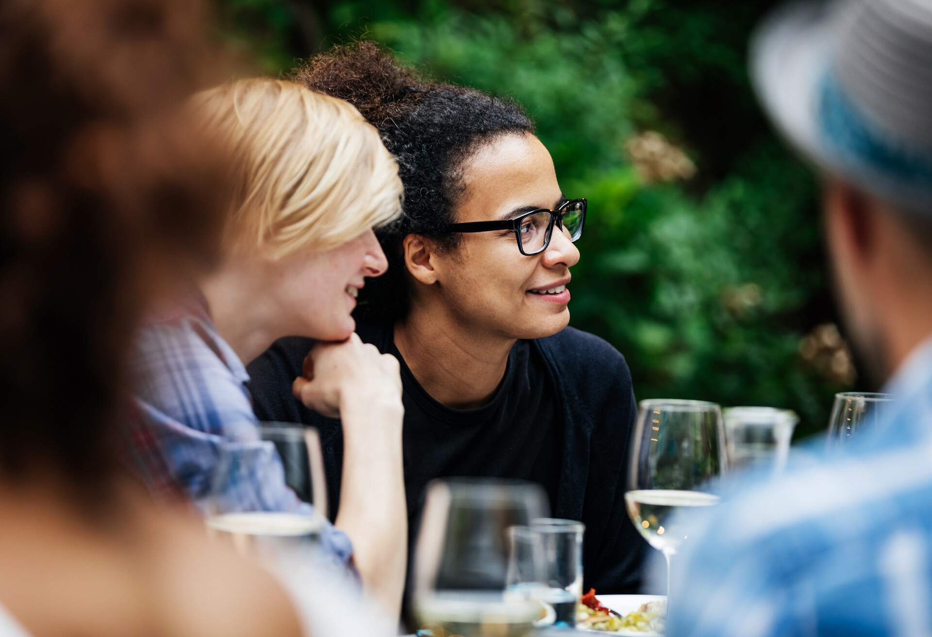 A group of frineds sitting down at a table, drinking with their family at a barbecue.