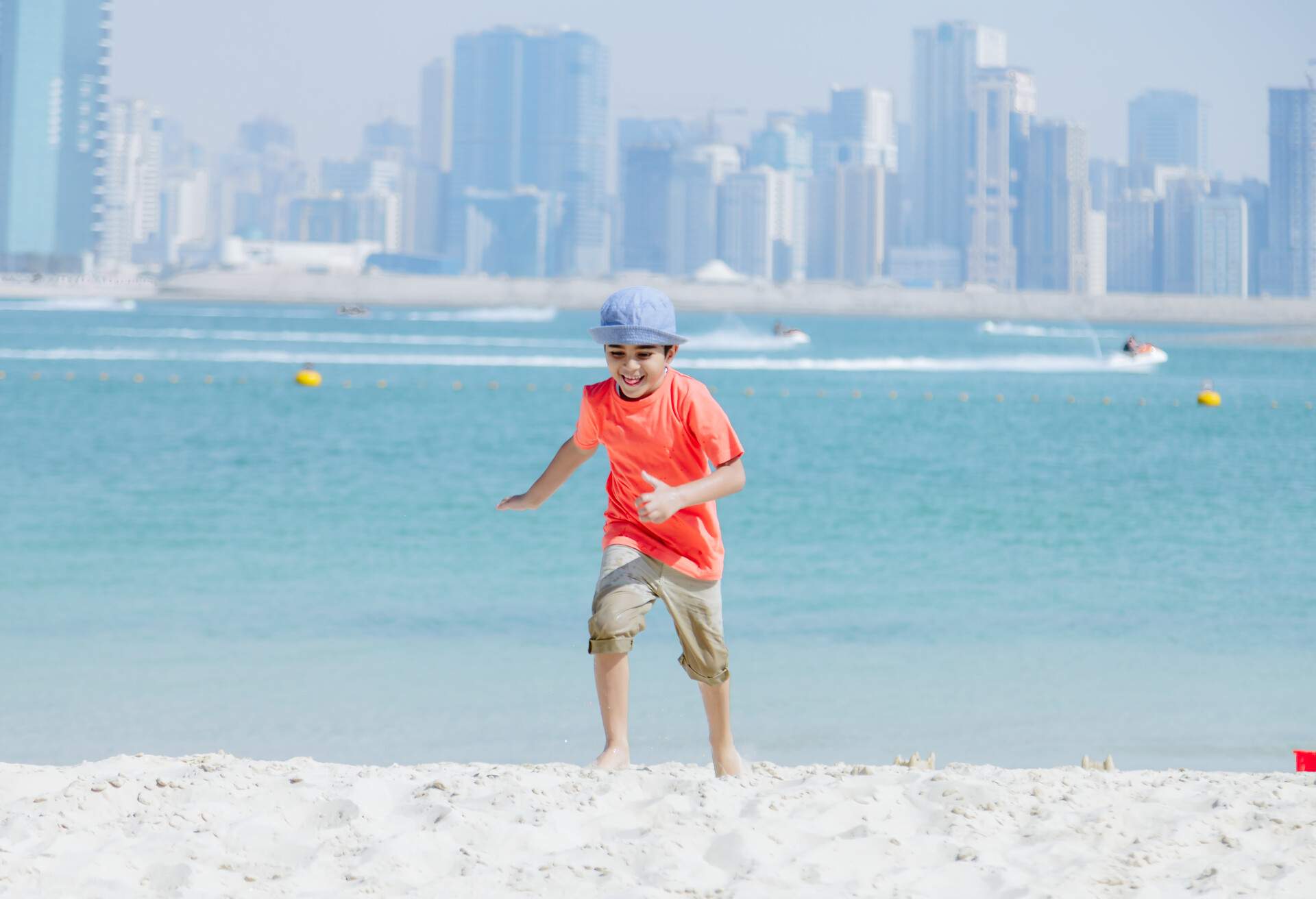 Cheerful middle eastern little boy running and having fun on sandy beach like an airplane