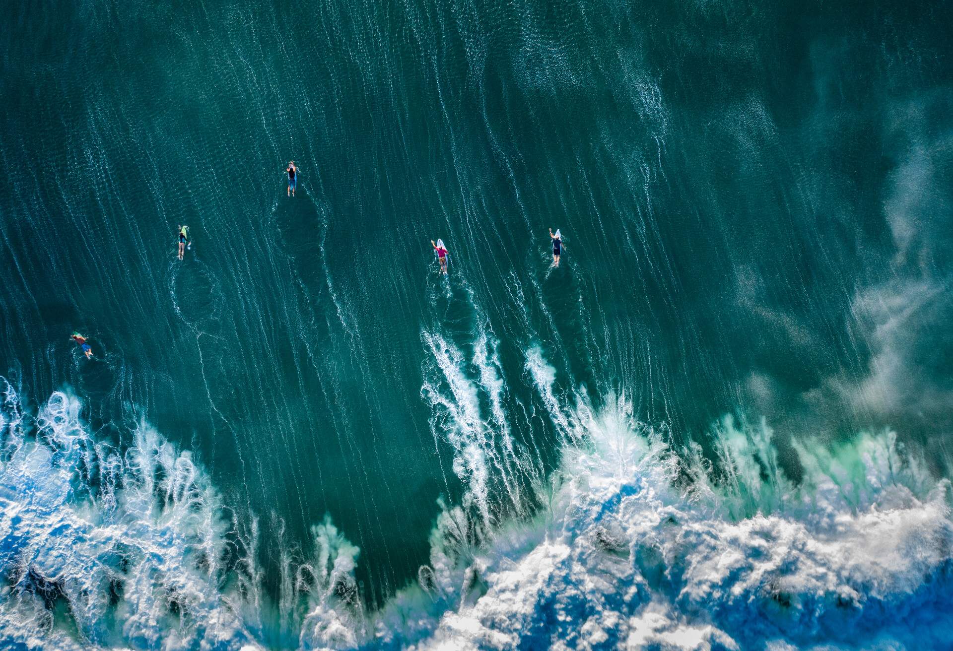 View directly above of a small group of surfers paddling through massive tidal waves to capture the next waves in Bali Indonesia.