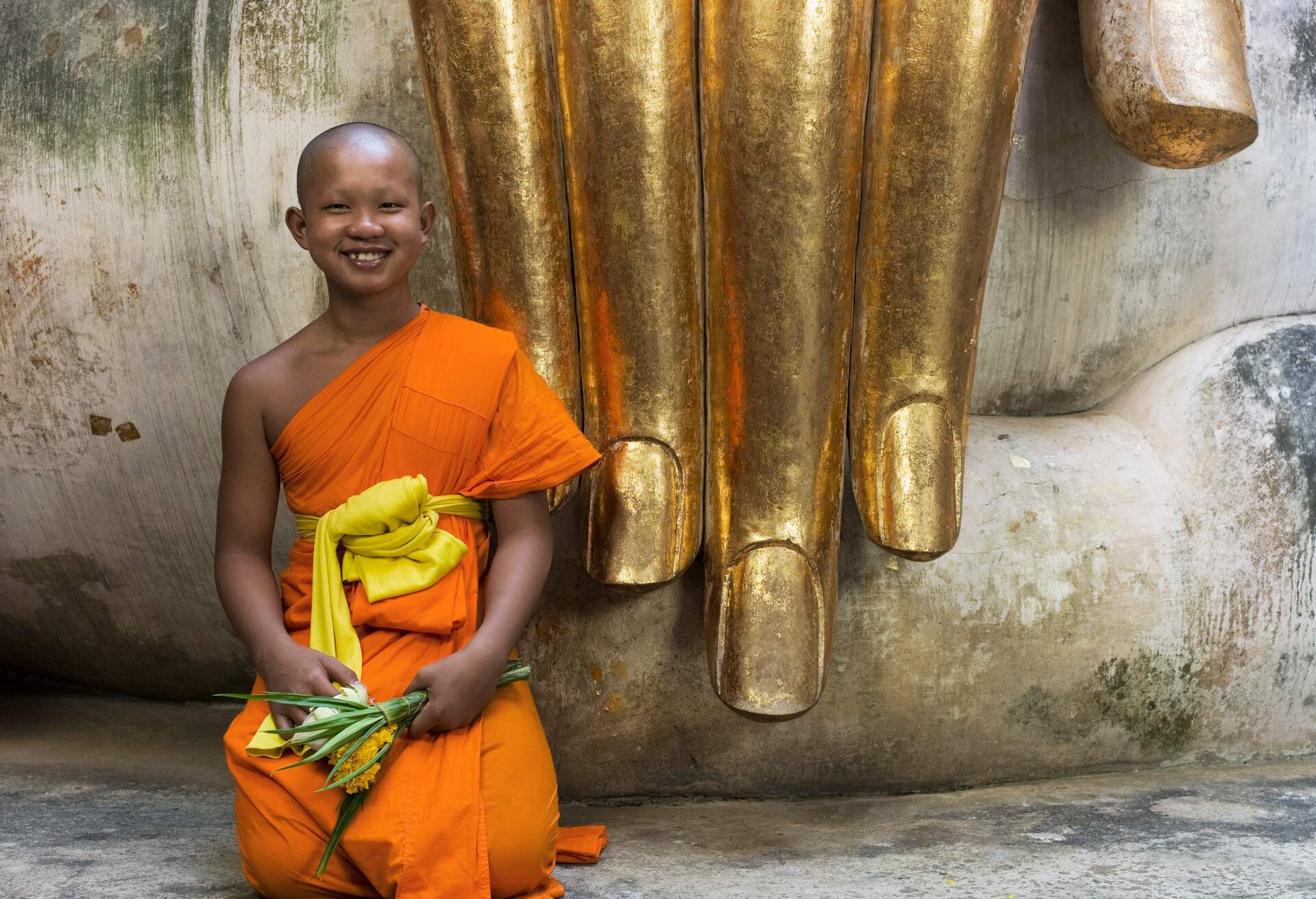 Thailand, Sukothai, Wat Si Chum, portrait of Buddhist monk in front of seated Buddha and golden hand.