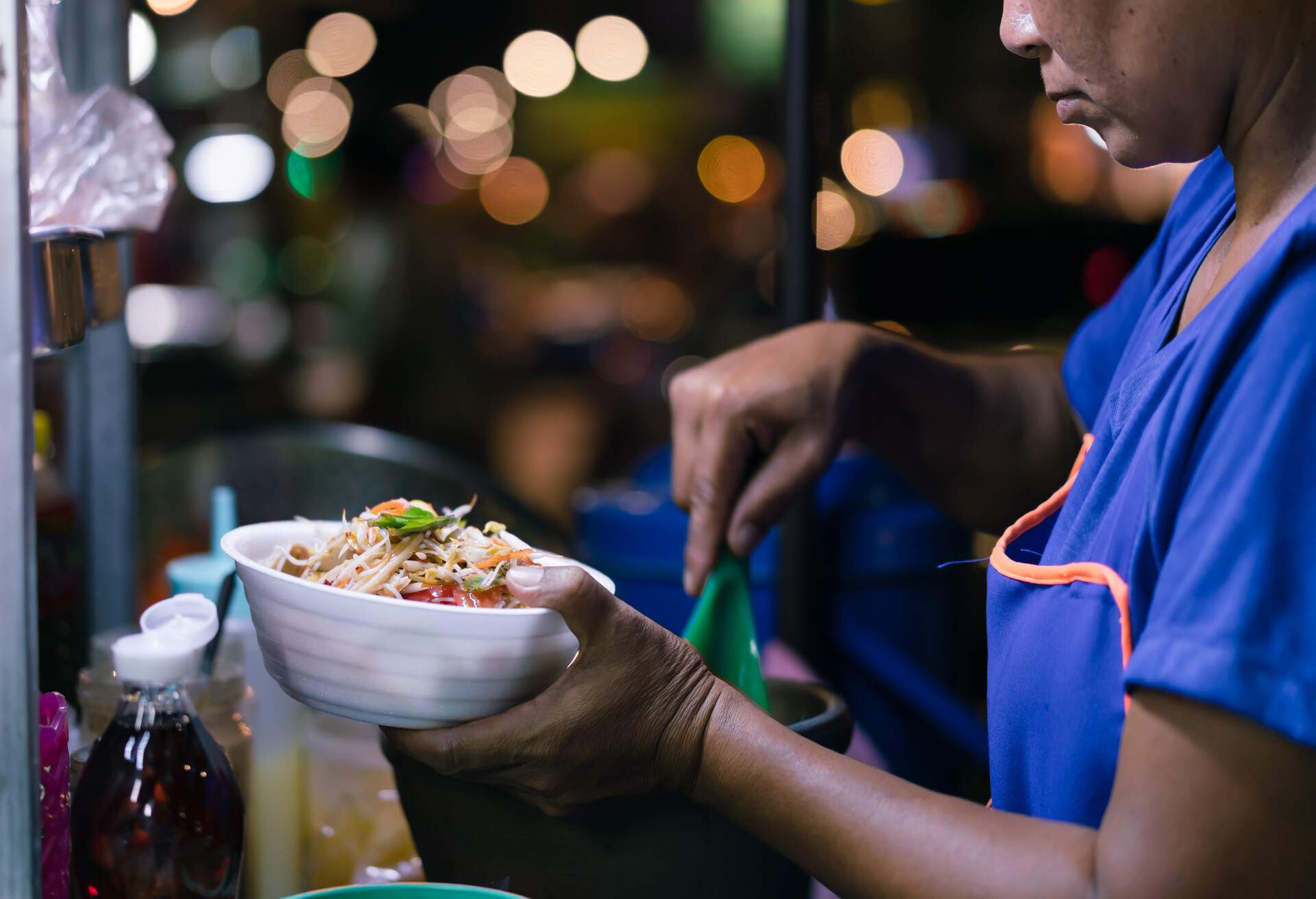 Street food chef preparing spicy green papaya salad - Woman serving Som Tum Thai food  at night market with bokeh - Traditional meal served on the street - Homemade, Business and Asian cuisine concept