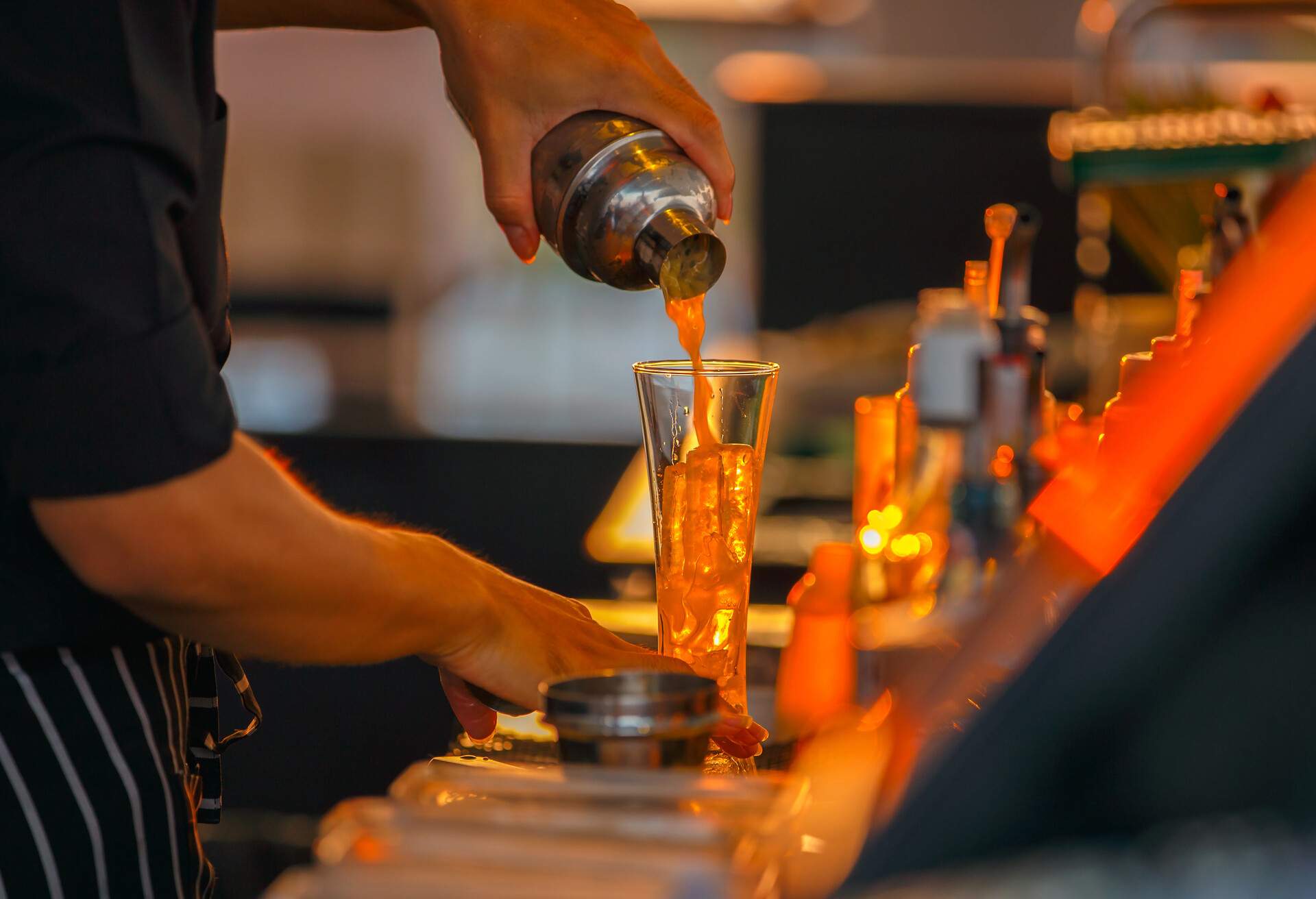 Close up left hand bartenders in process of preparing orange juice for customers who order from rooftop bar and restaurant.