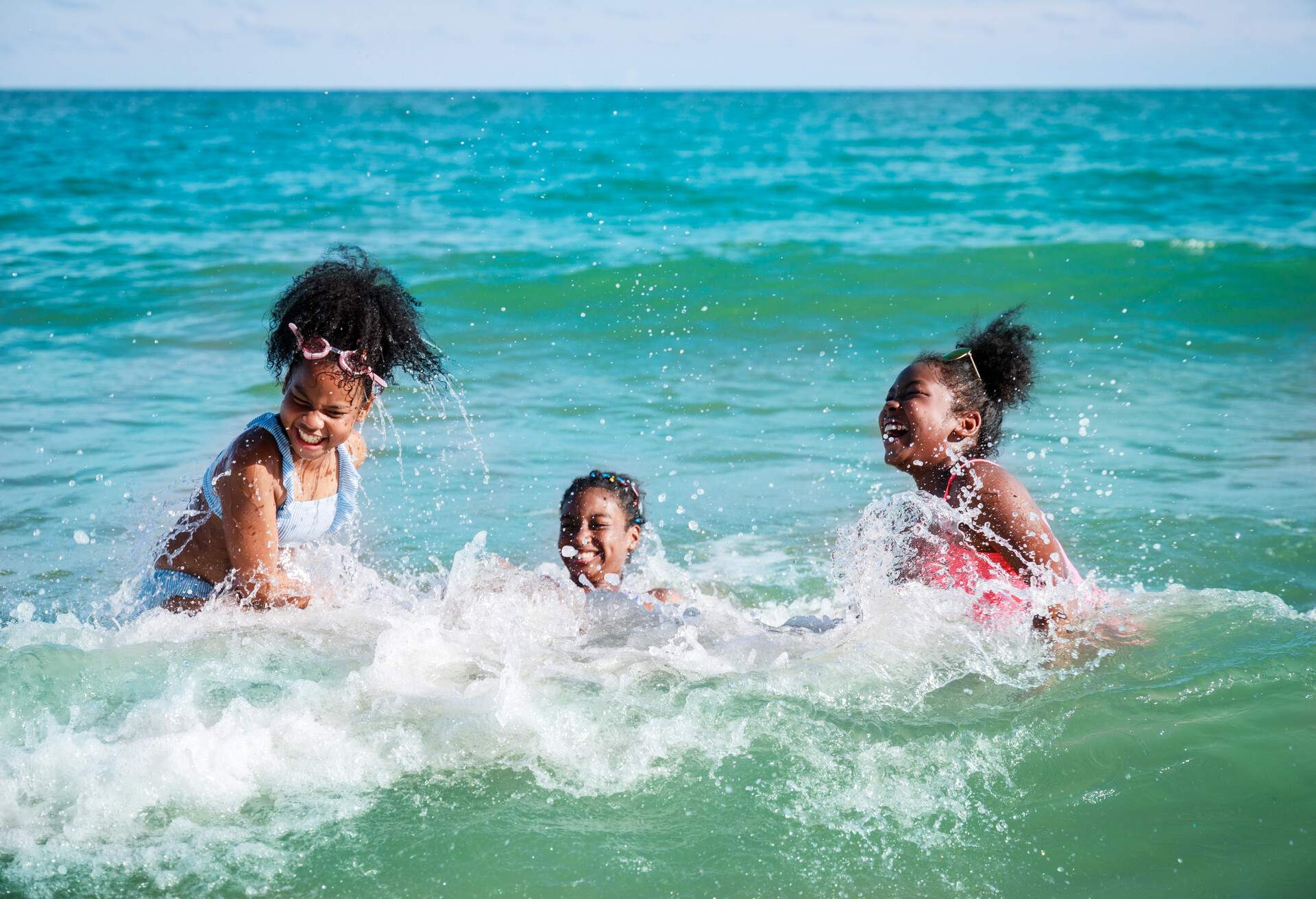 Happy three African American kids are swimming in the sea playfully together. With waves and splashes of water. Happy friendship. Happy vacation holiday. Relaxation in vacation in the summer concept.