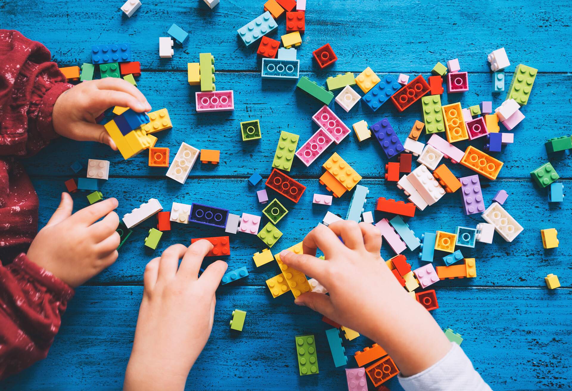 Children play and build with colorful toy bricks or plastic blocks on table. School or preschool background. Concept of kids leisure and education at home or class, early learning and development.