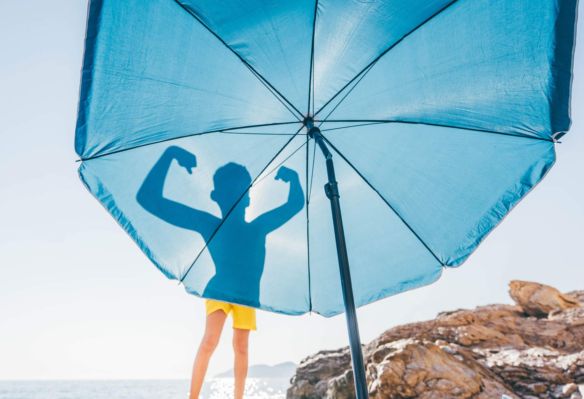 Silhouettes of boy flexing his muscles on blue beach umbrella.