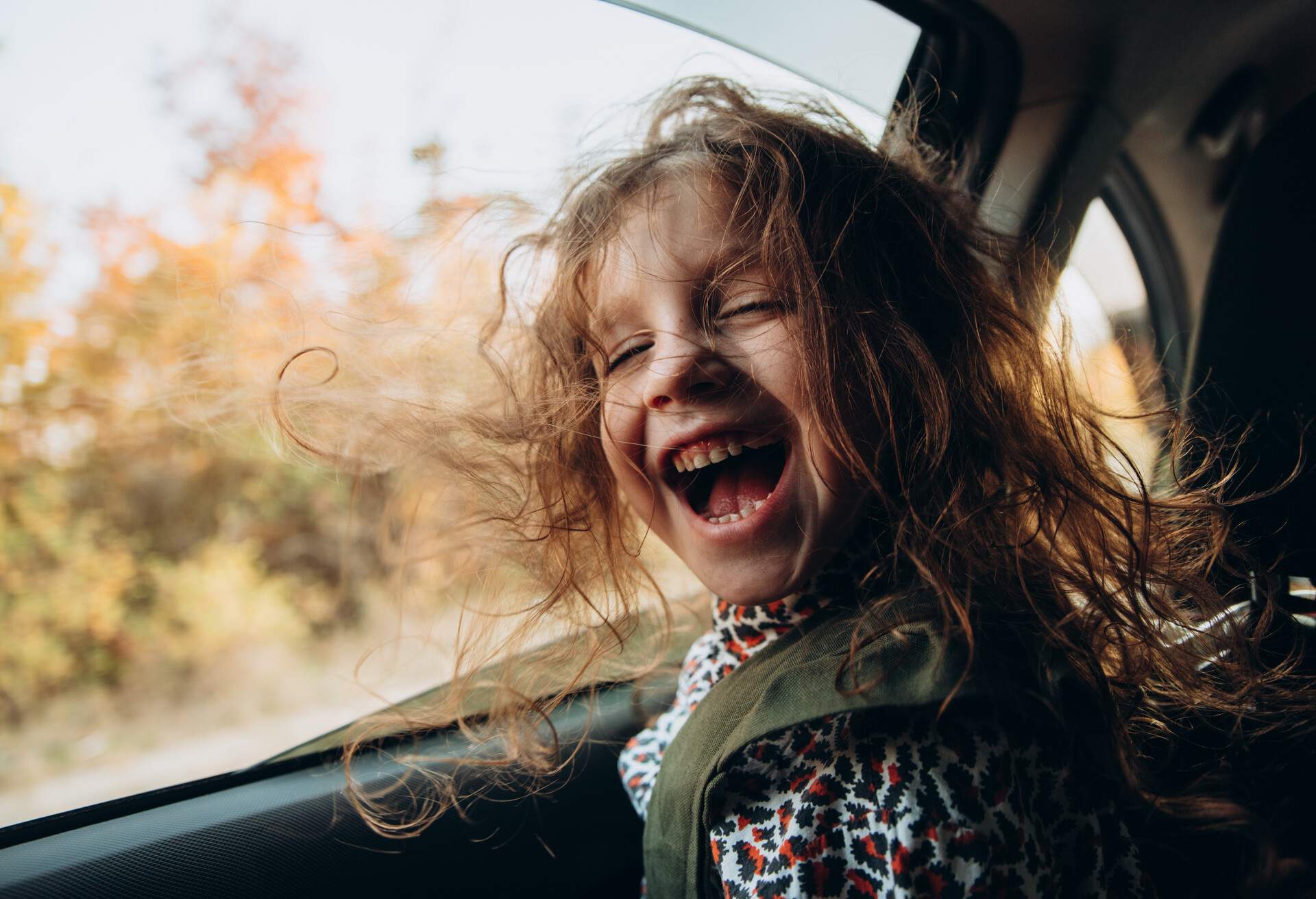 Little curly-haired laughing smiling girl sitting in the car and looking at the camera. The daughter travels with her parents.