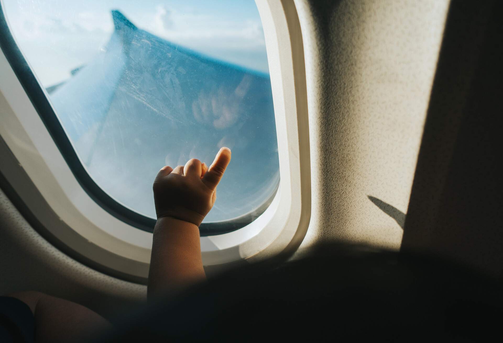 Cropped hand of a toddler pointing airplane window against blue sky while travelling