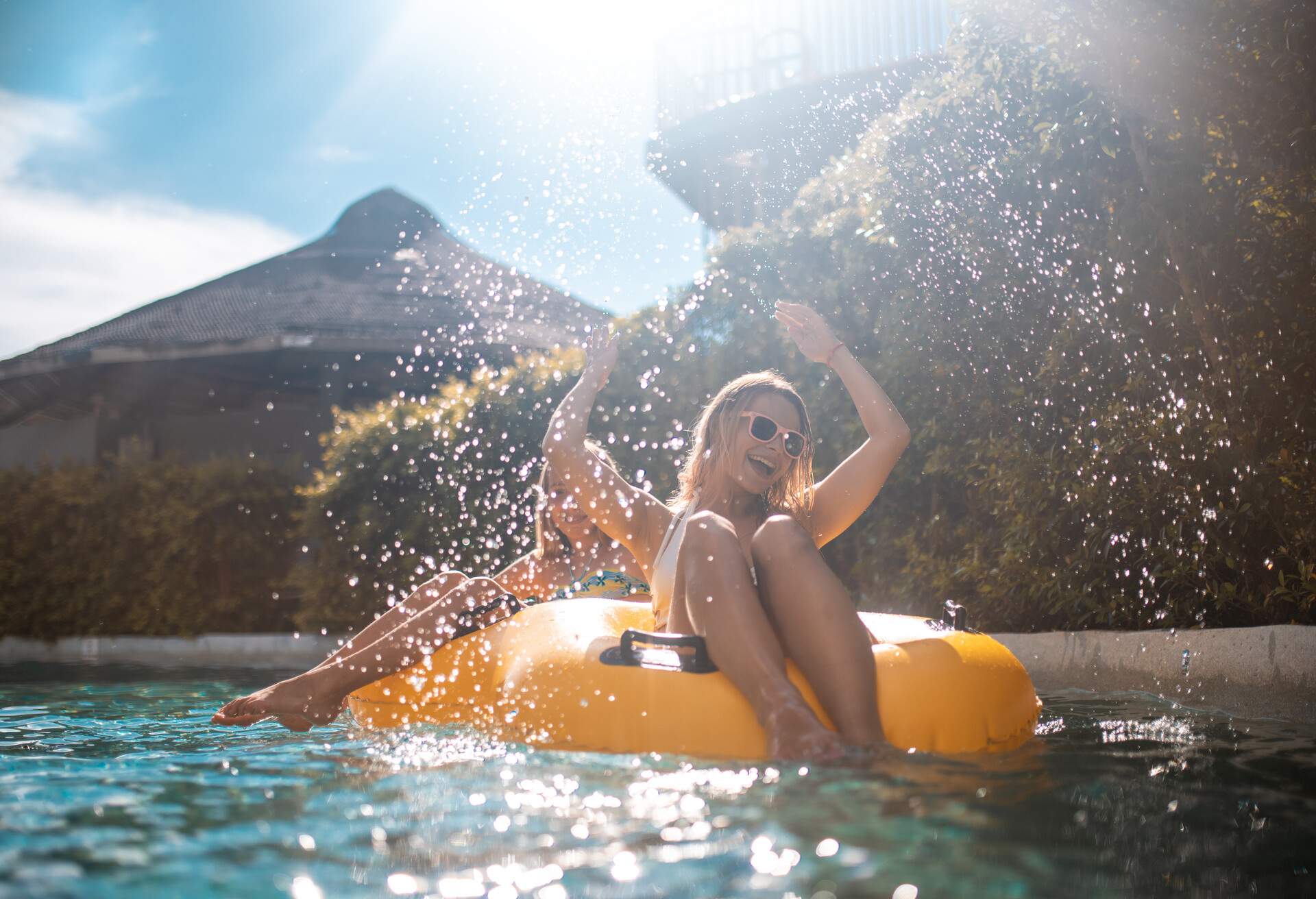 Smiling sisters relaxing on yellow inflatable ring at water park. They are floating in swimming pol. They are enjoying summer vacation.