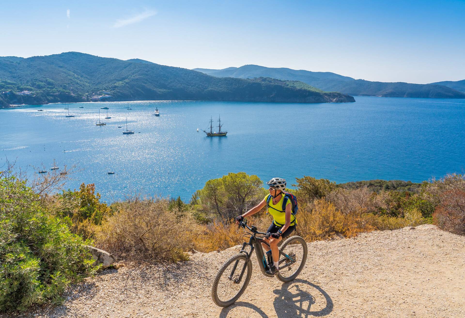 nice woman riding her electric mountain bike on the coastline above the mediterranean sea on the Island of Elba in the tuscan Archipelago, Tuscany, Italy