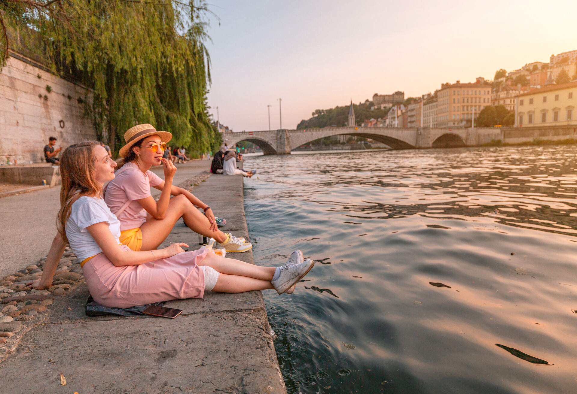 Two happy caucasian and asian girls friends meeting great sunset on a river Saone in Lyon city. Travel and lifestyle in France