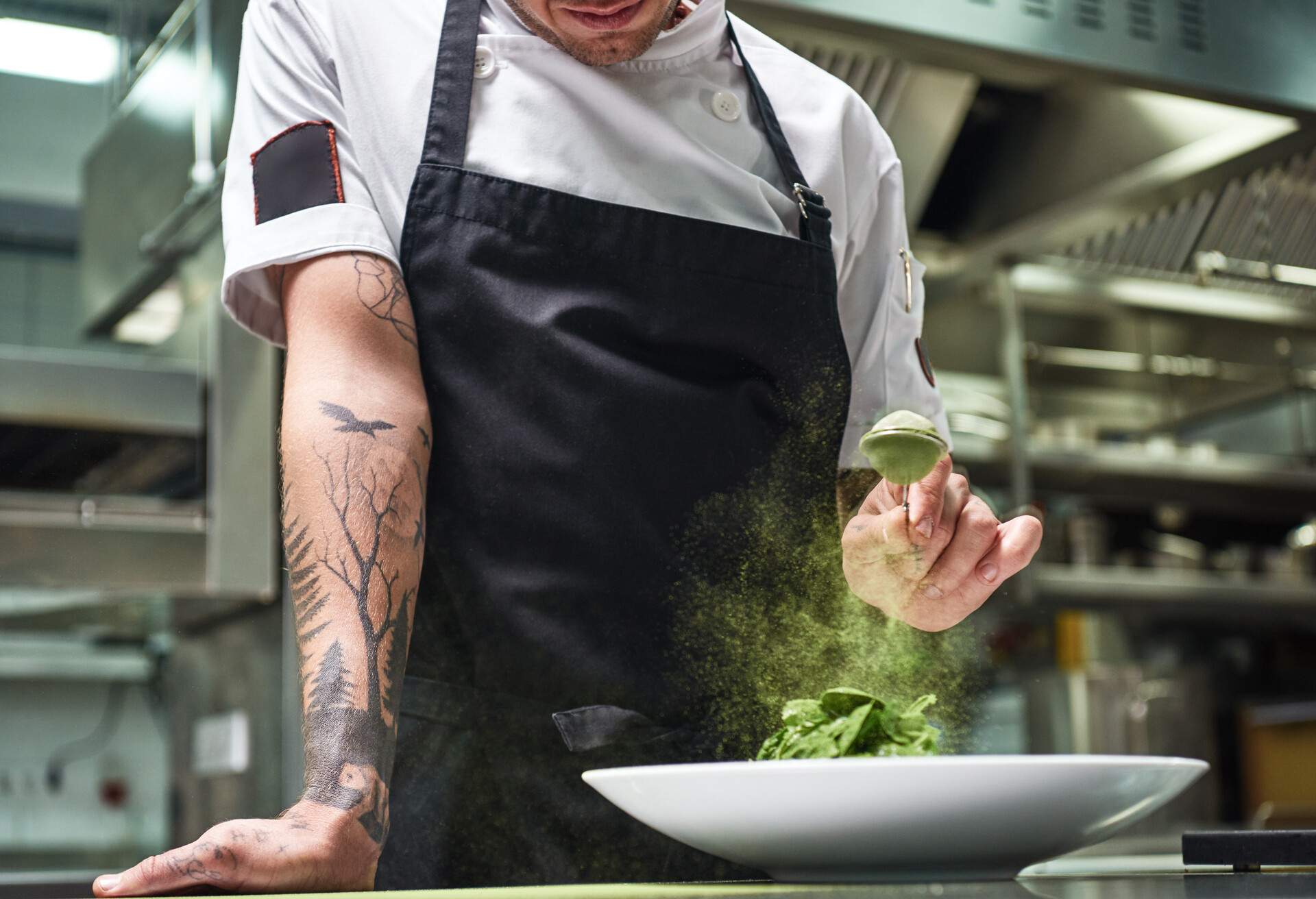 Slow motion. Cropped image of chef's hands with tattoos adding spices in salad while standing in a restaurant kitchen. Food concept. Food conept.