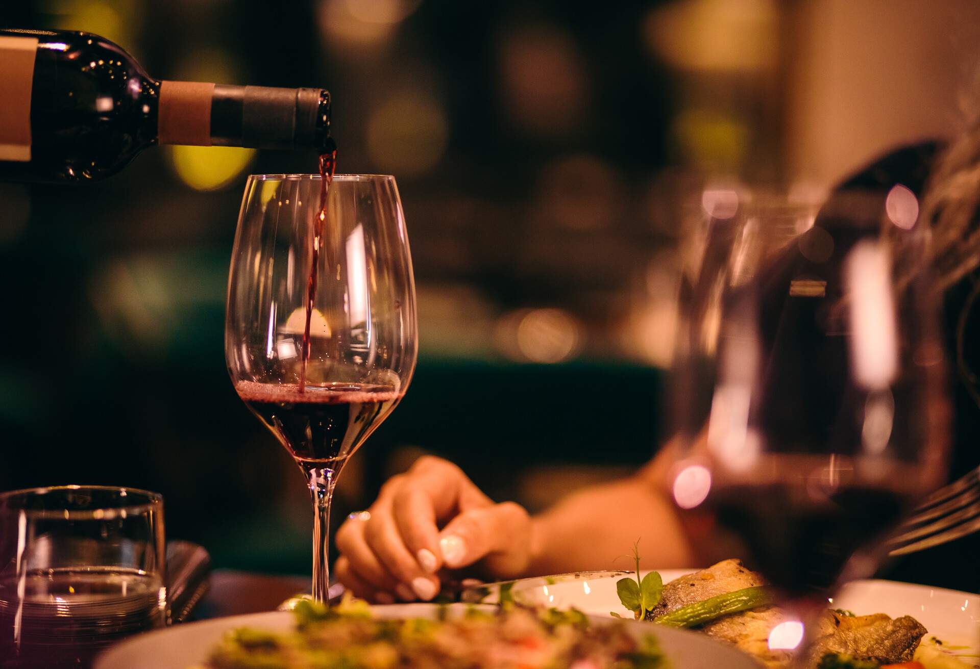 Close-up of waiter holding bottle and serving red wine during dinner at luxurious gourmet restaurant