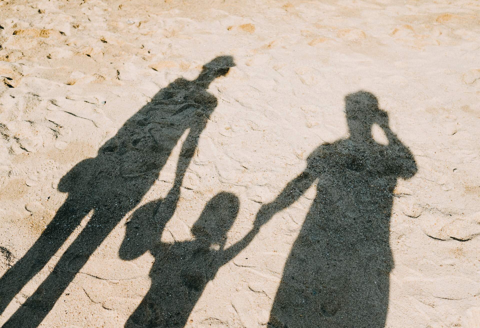 Shadow on sandy beach of a loving family of three holding hands relaxing on a lovely sunny day