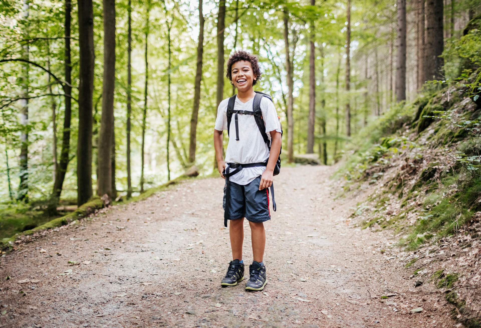 A portrait of a young boy smiling while out hiking a woodland trail in the afternoon.