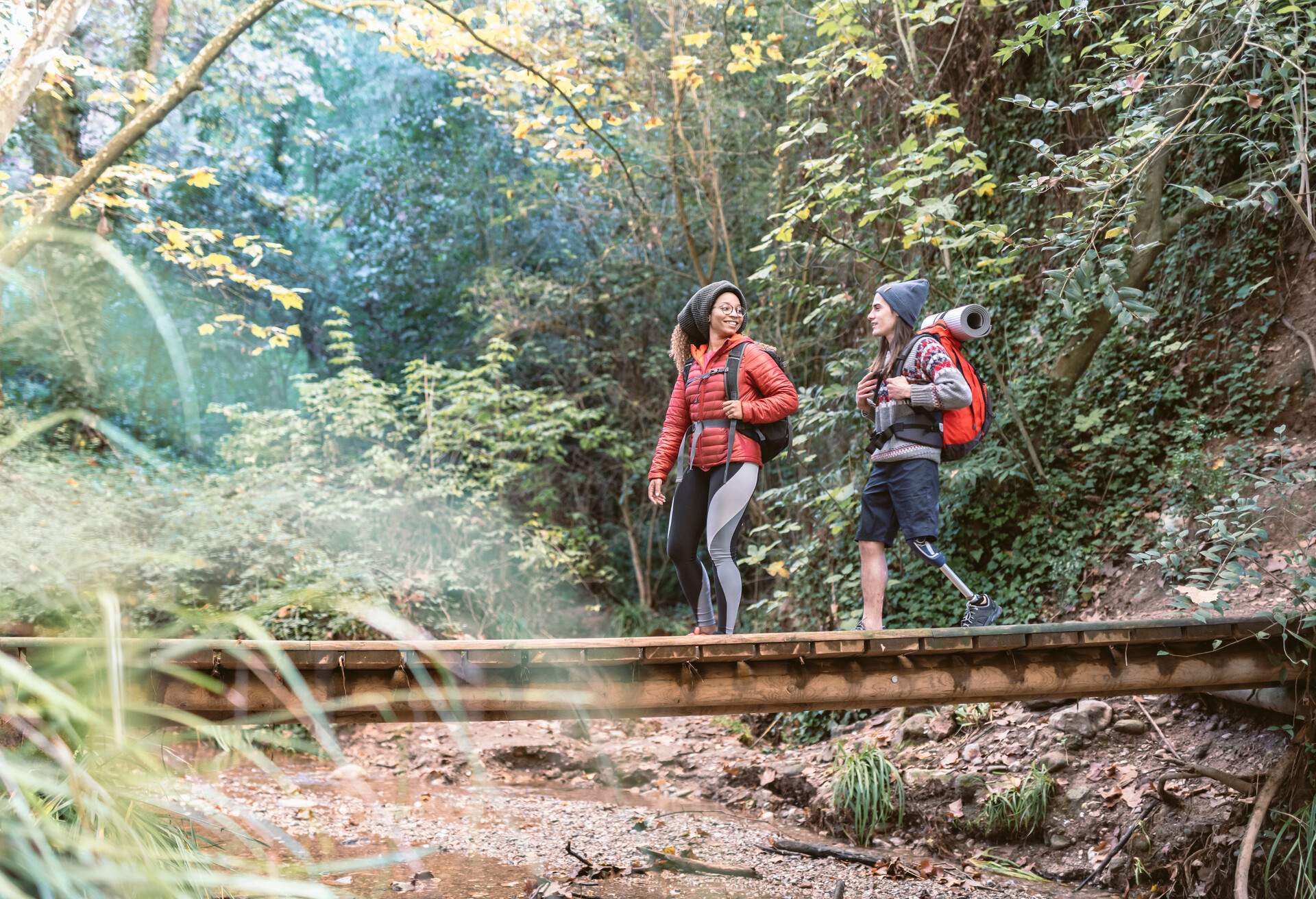 Happy backpacker couple walking on a wooden bridge while enjoying a hike on the woods. Disabled man with a prosthetic leg.