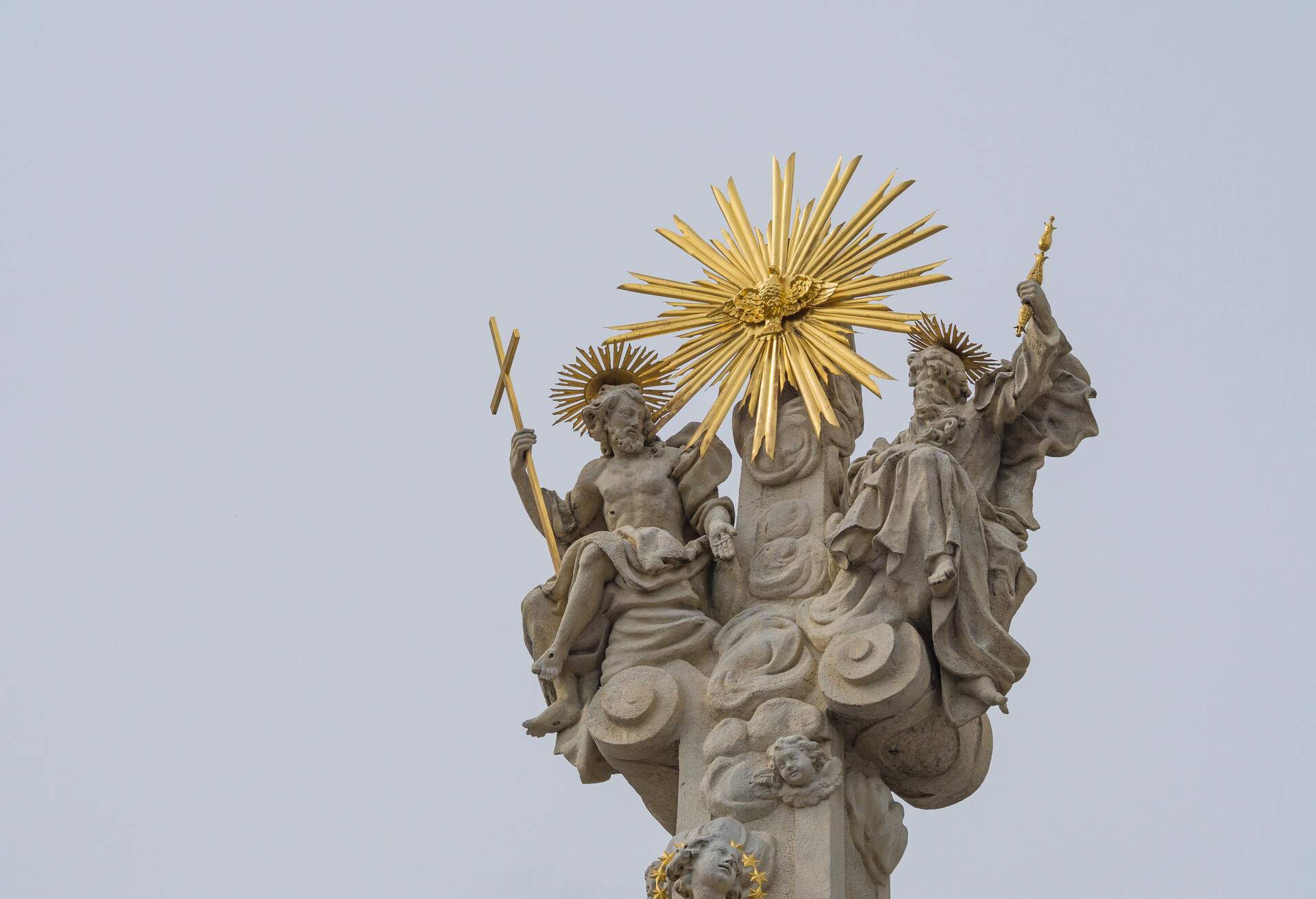 top of baroque plague column monument with saint peter and saint paul and golden sun in Olomouc city on light sky background