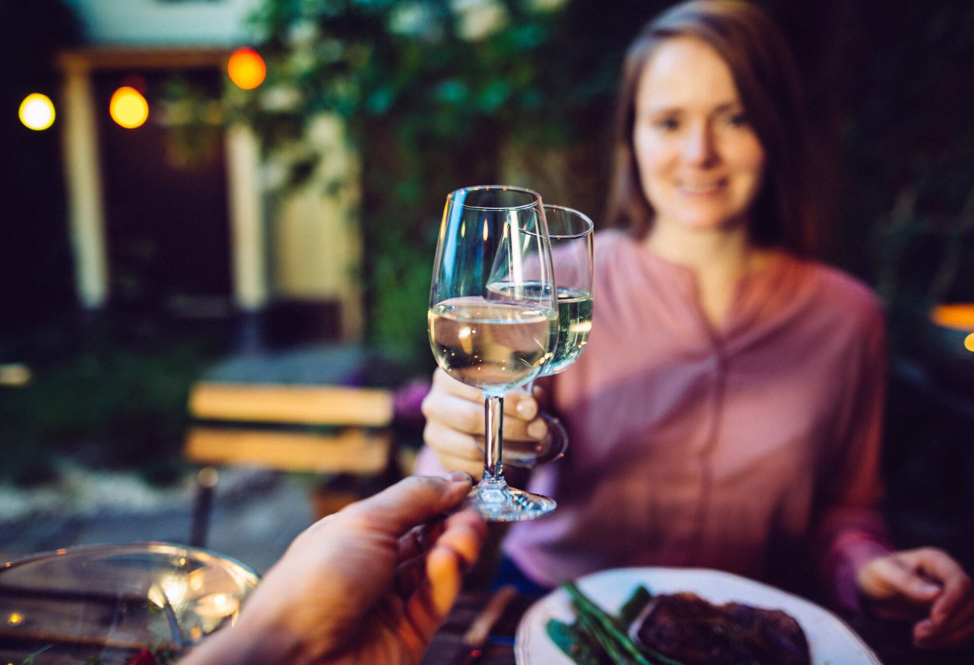 Couple cheering with glass of wine while having a romantic dinner outdoor.