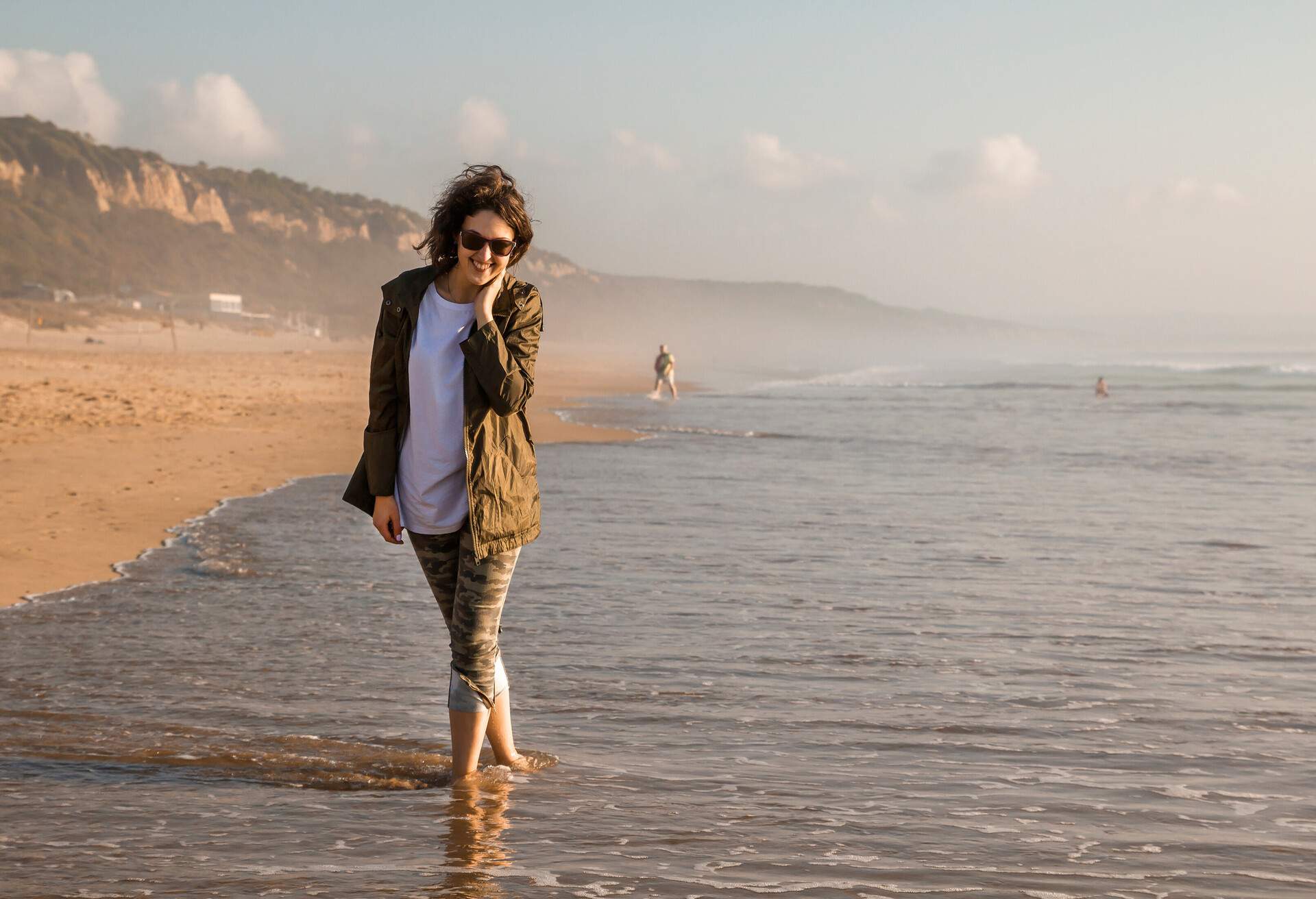 Portrait of young and stylish woman standing on the beach during sunset. Calm water around. Lisbon, Portugal.; Shutterstock ID 1038657952; Purpose: Content; Brand (KAYAK, Momondo, Any): Any