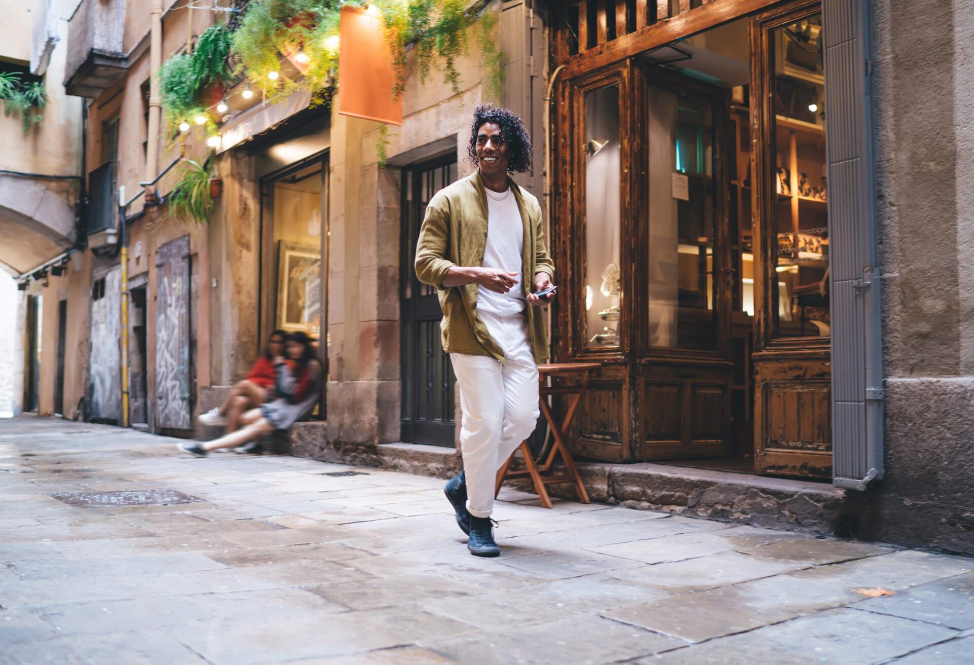 Full body of cheerful young ethnic male traveler in casual clothes smiling and looking away while exploring narrow street of Barcelona