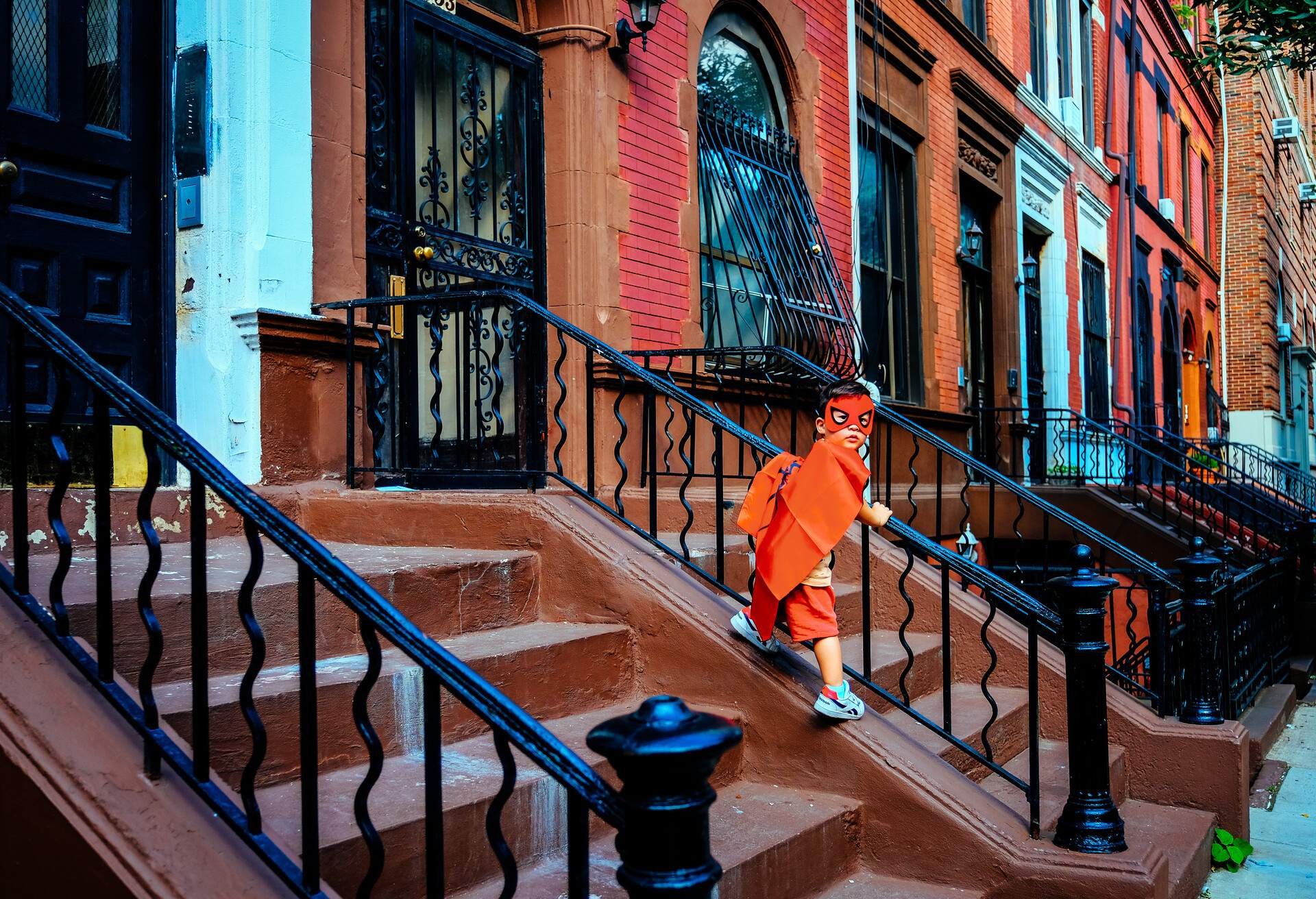 A child dressed as a superhero plays on the stairs of a brownstone building in New York City.