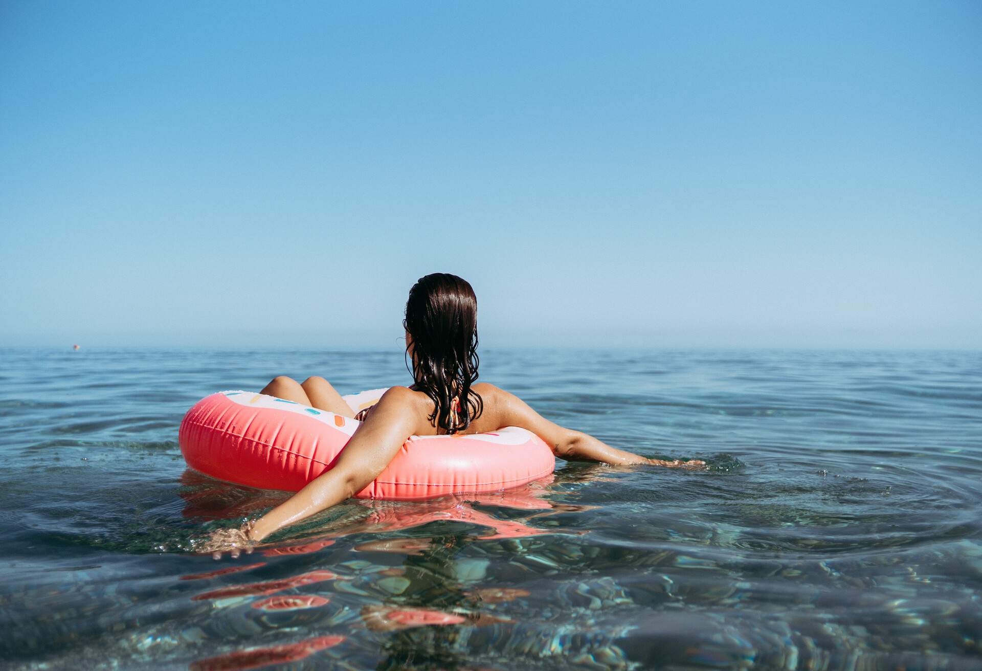 Young woman in a sprinkled doughnut float at the beach. Sunset summertime