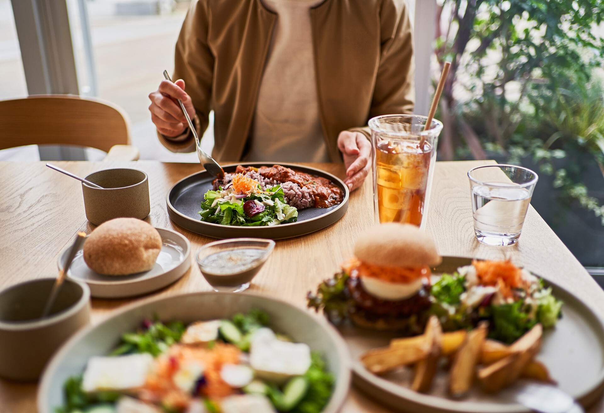 Vegan cafe lunch at Vegan Cafe. .Organic curry, alternative soy meat burger, tofu salad..Houjicha iced tea is made with recycled paper straws..The woman sitting in the back is eating an organic vegan curry.