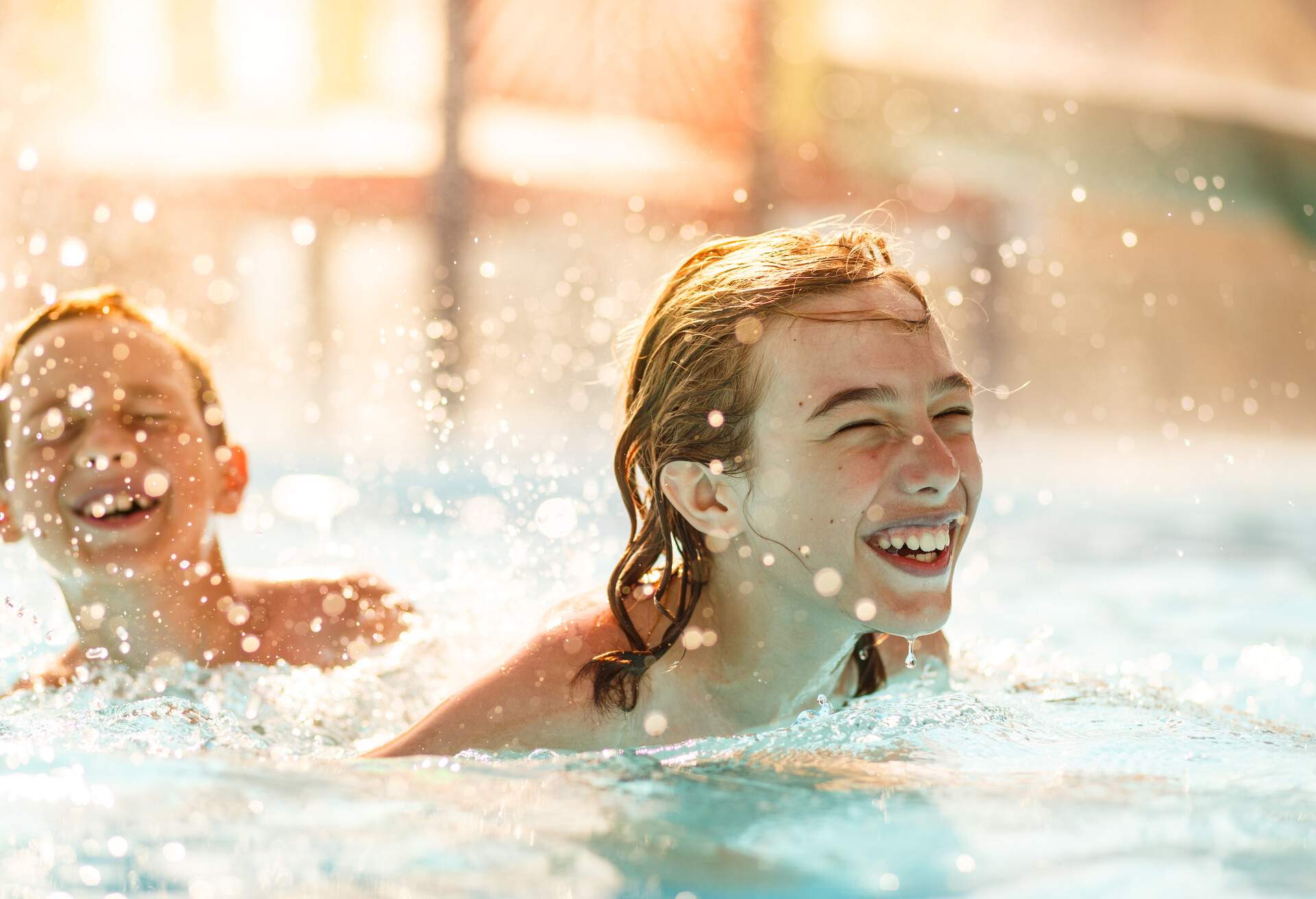 Two boys are laughing while swimming in the pool on a hot day.