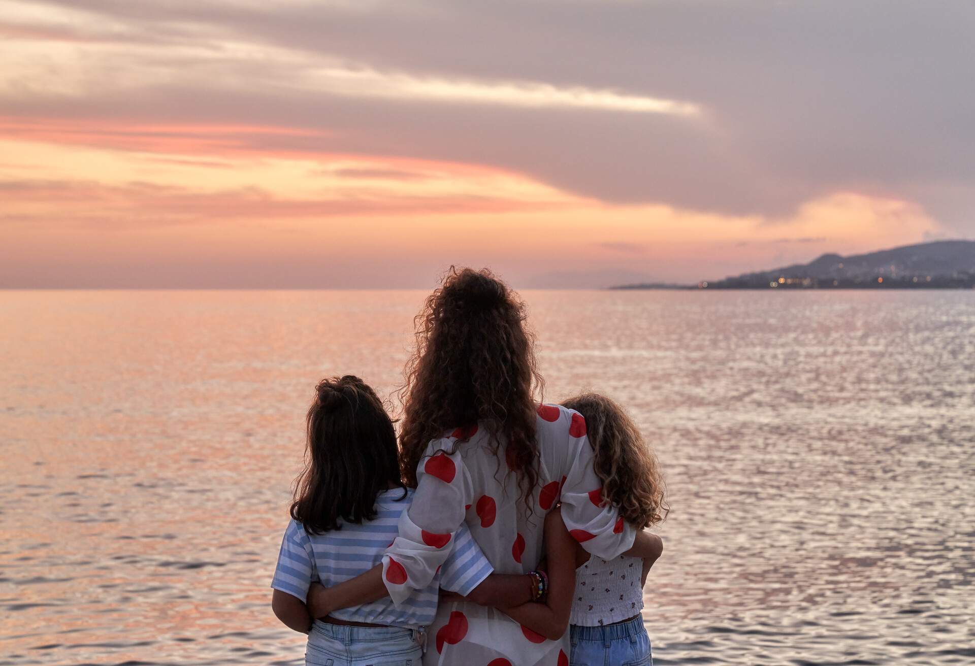 Rear view of single mother and two daughters watching sunset in the sea