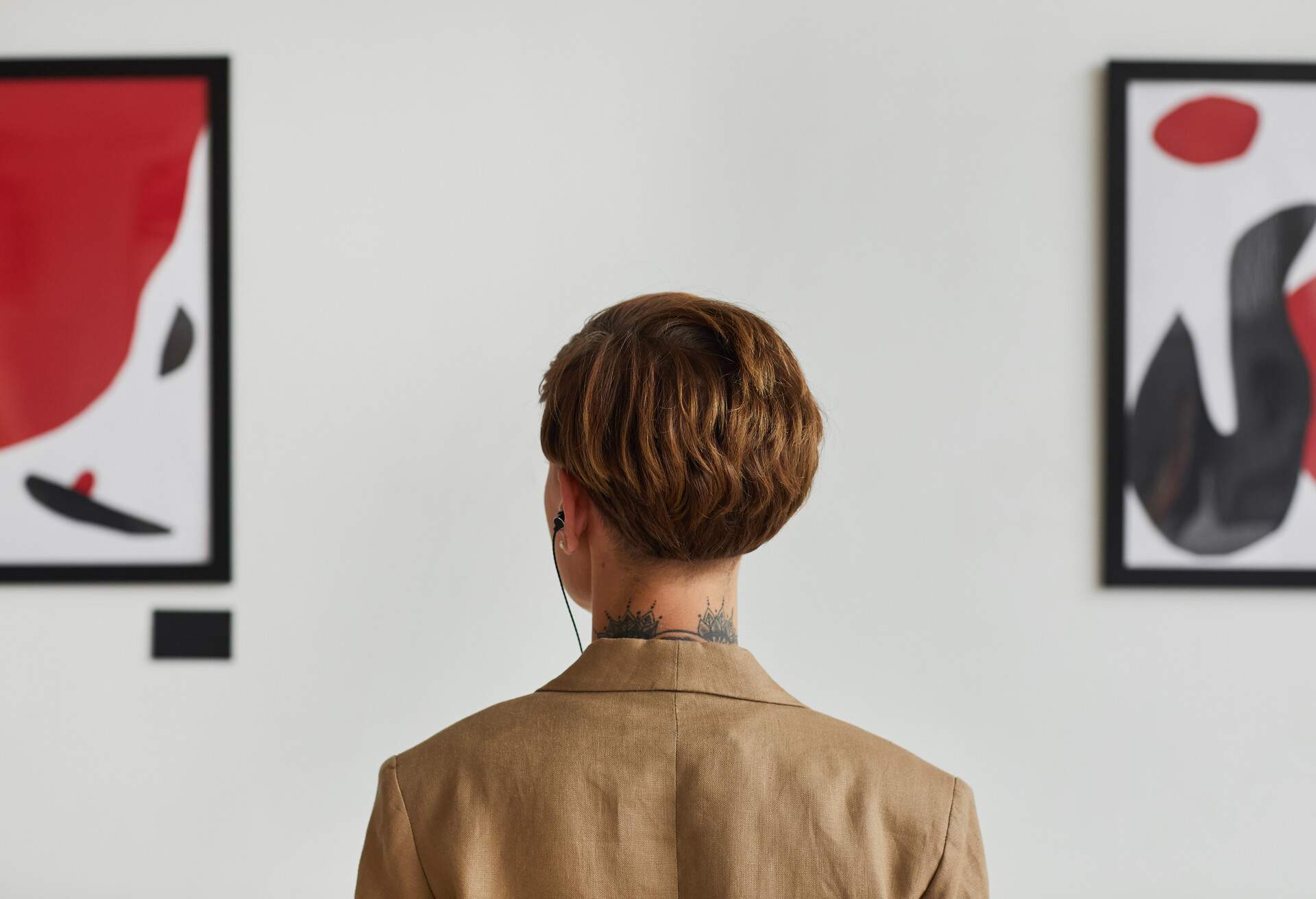 Graphic back view portrait of tattooed young woman looking at paintings and listening to audio guide at modern art gallery exhibition, copy space