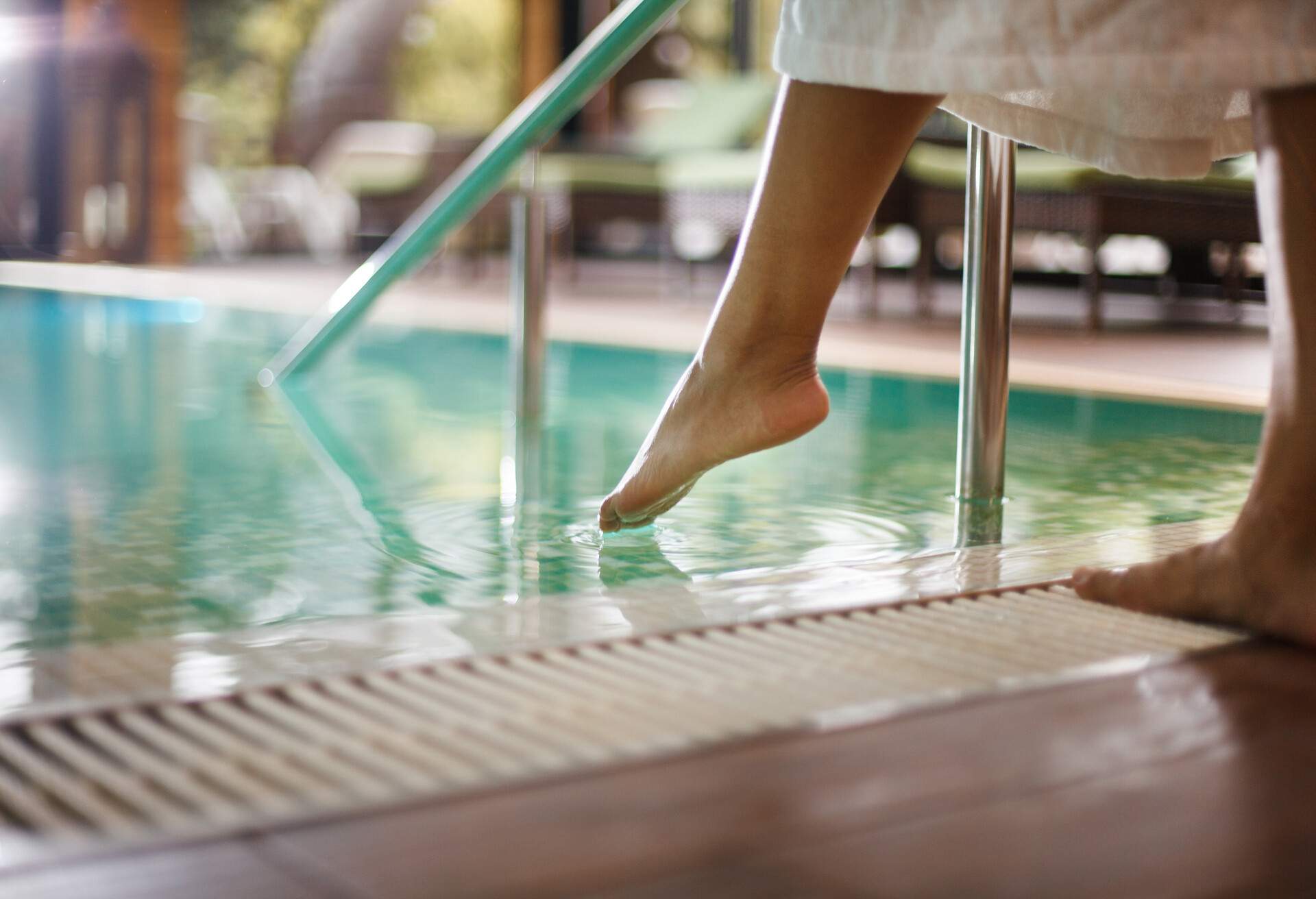 Low section of a woman dipping toes into swimming pool at spa.