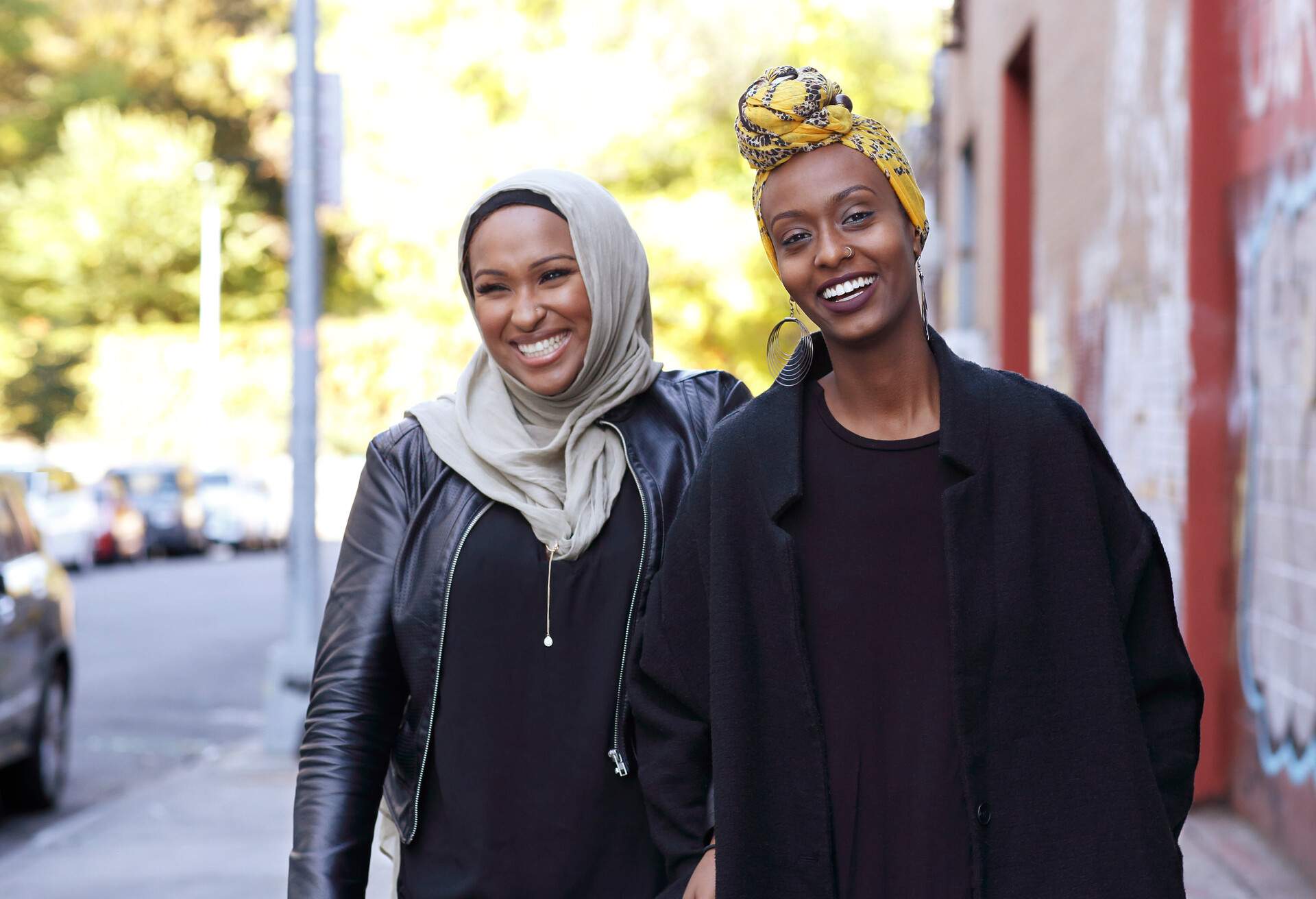 Two young, Muslim women walking down the street, laughing together.