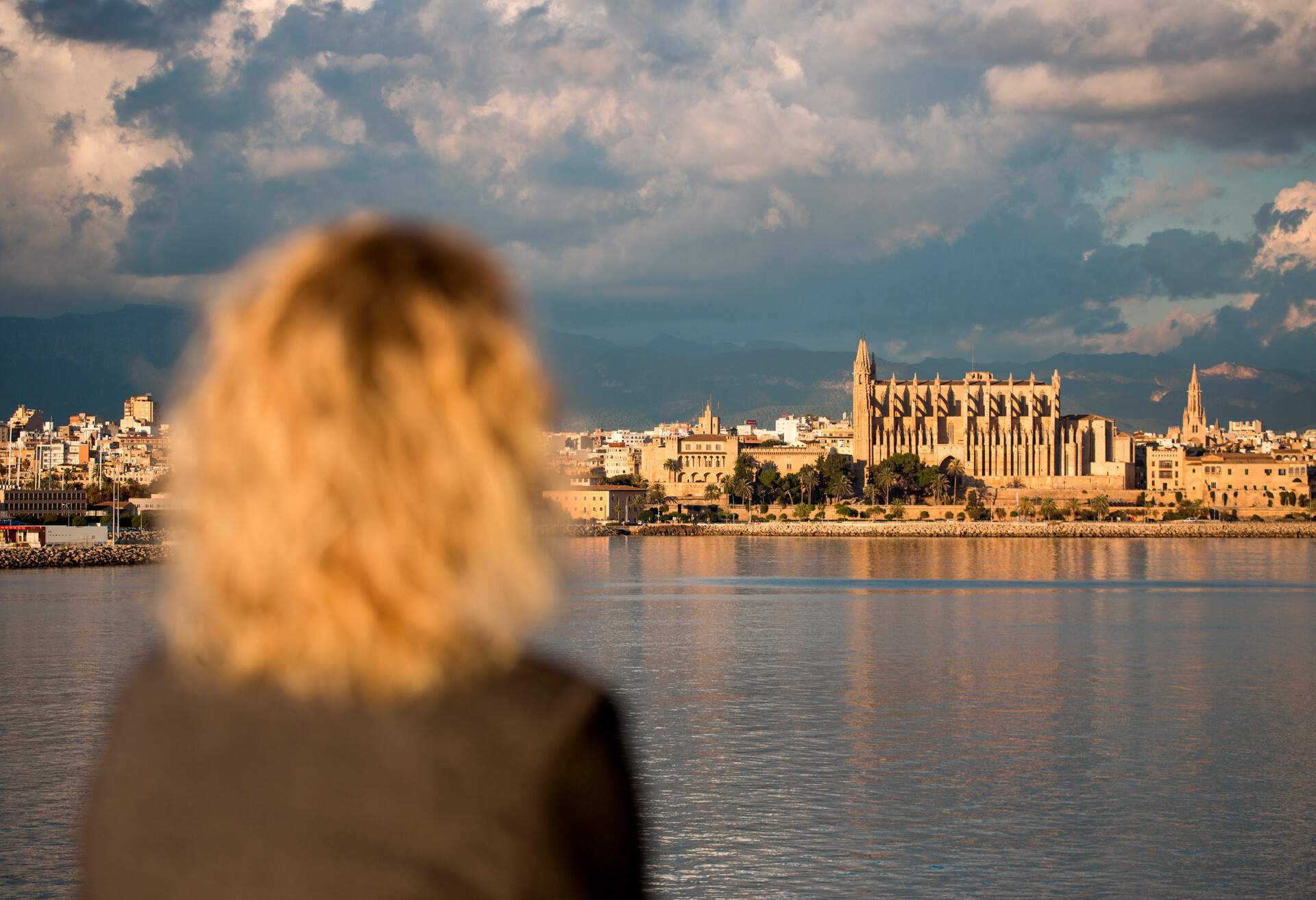 La Seu Palma Cathedral seen from the sea with out of focus blond woman in foreground, Palma, Mallorca, Balearic Islands, Spain.