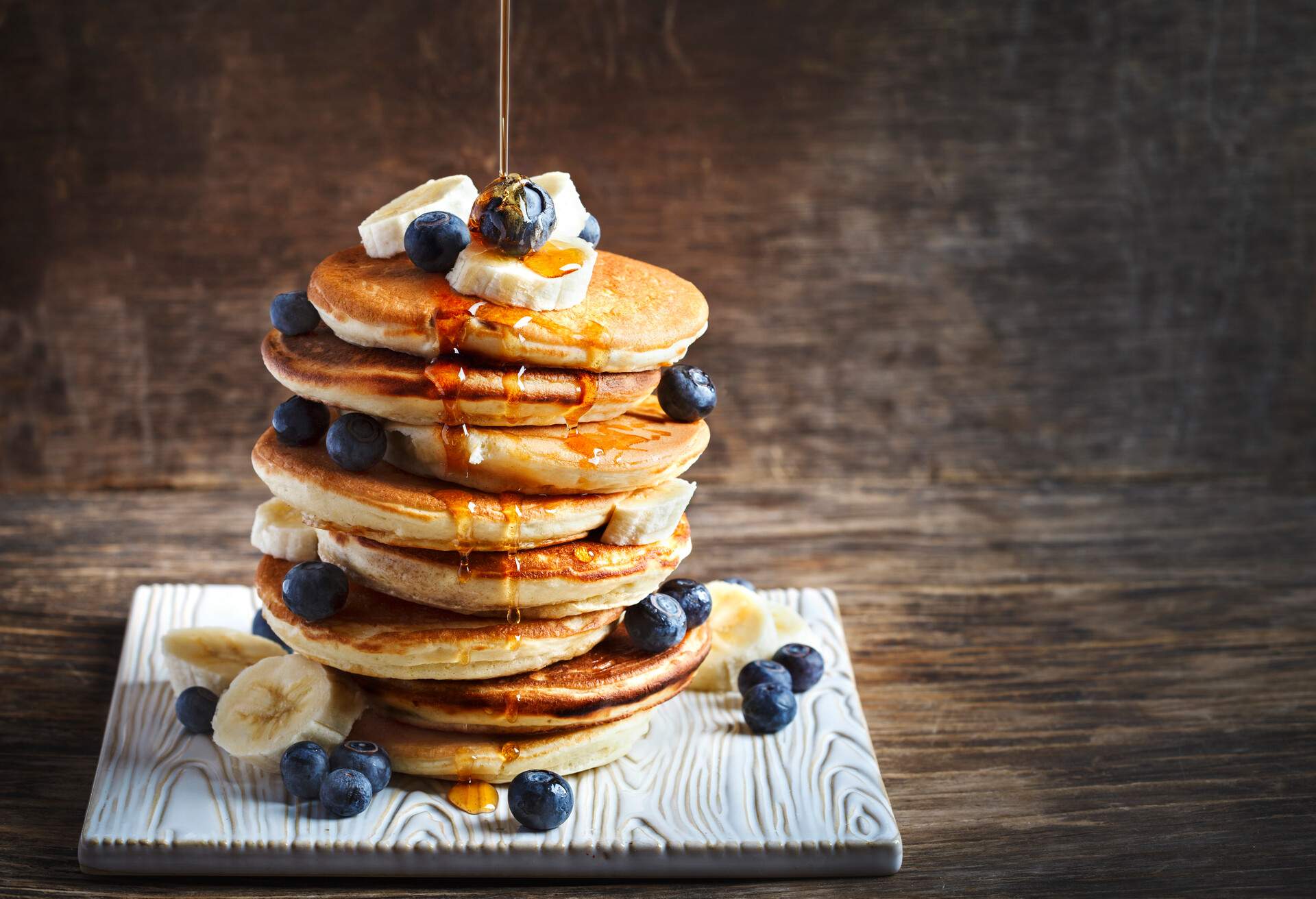 Pancakes with banana, blueberry and maple syrup for a breakfast, wooden background, copy space