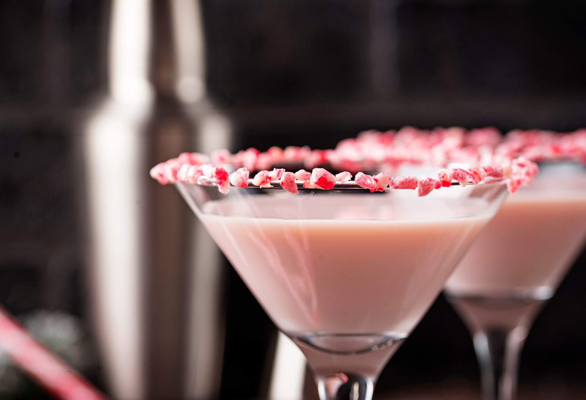 Two pink peppermint martinis with crushed candy canes on the rim of the glass