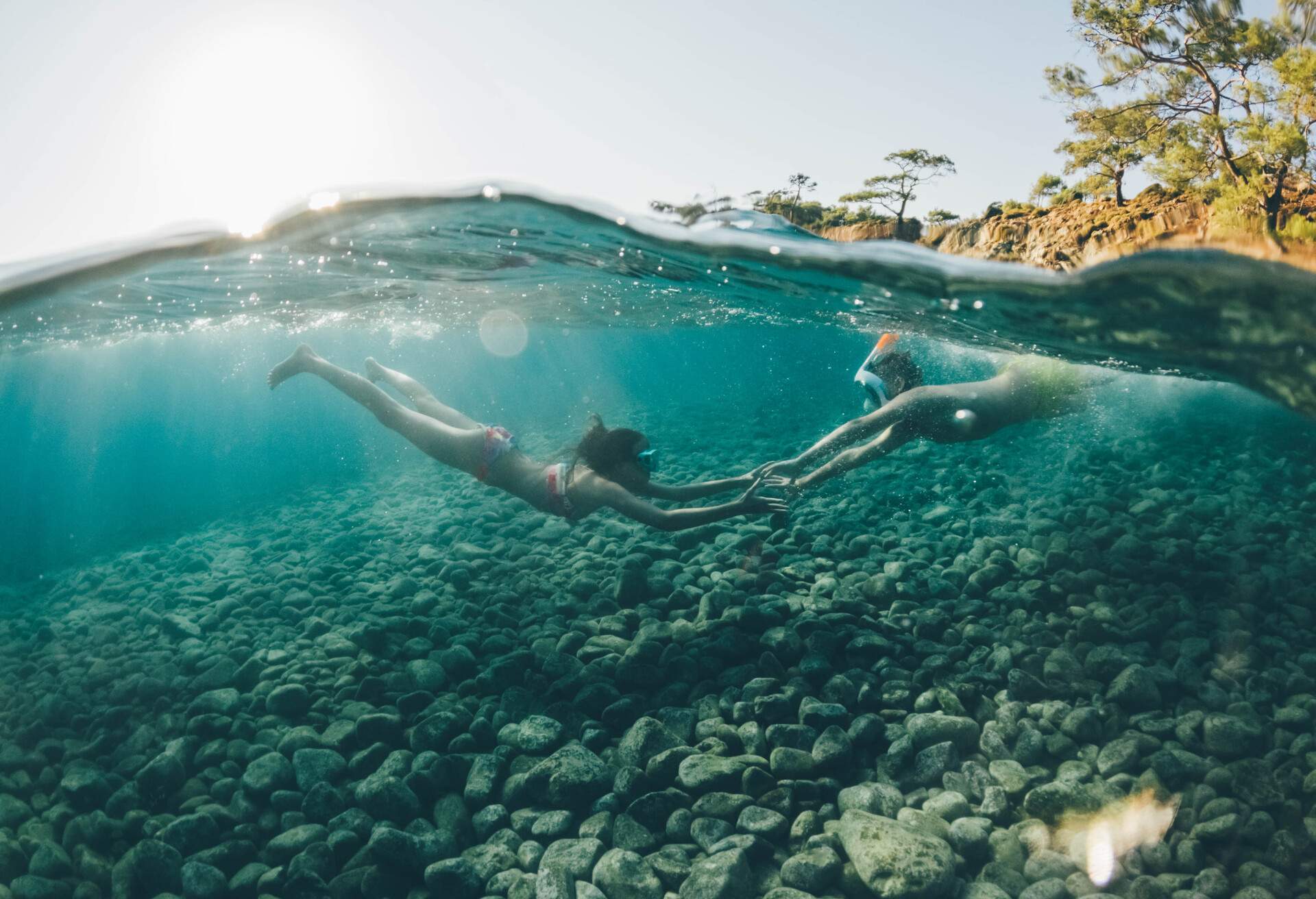 Children snorkelling and holding hands underwater with surface view