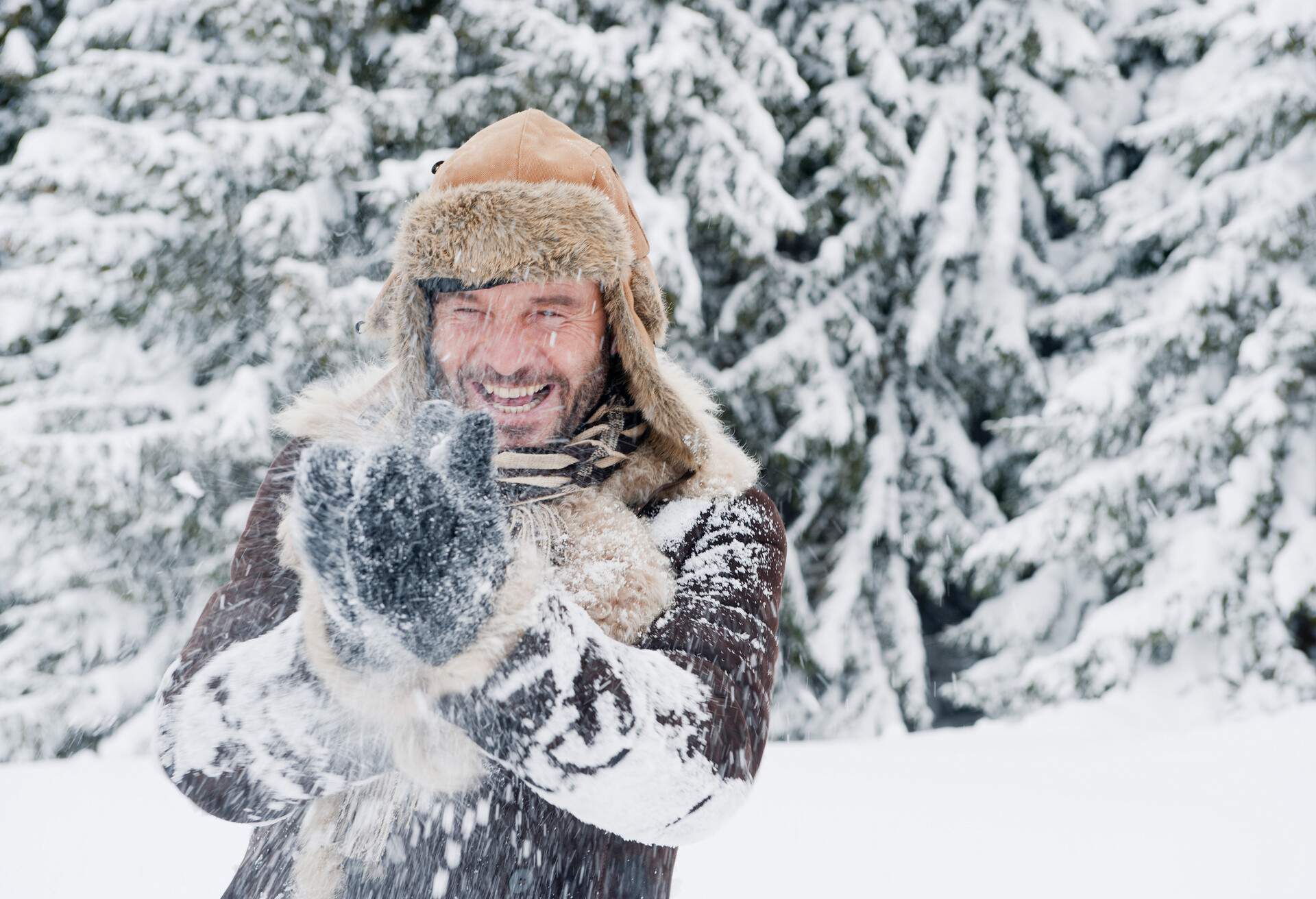 A man in winter clothes happily playing in the snow.