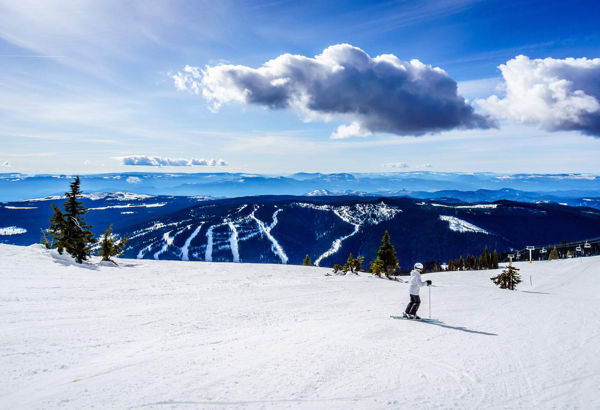 A skier skiing powder snow while looking at the bluish mountains and the sky.