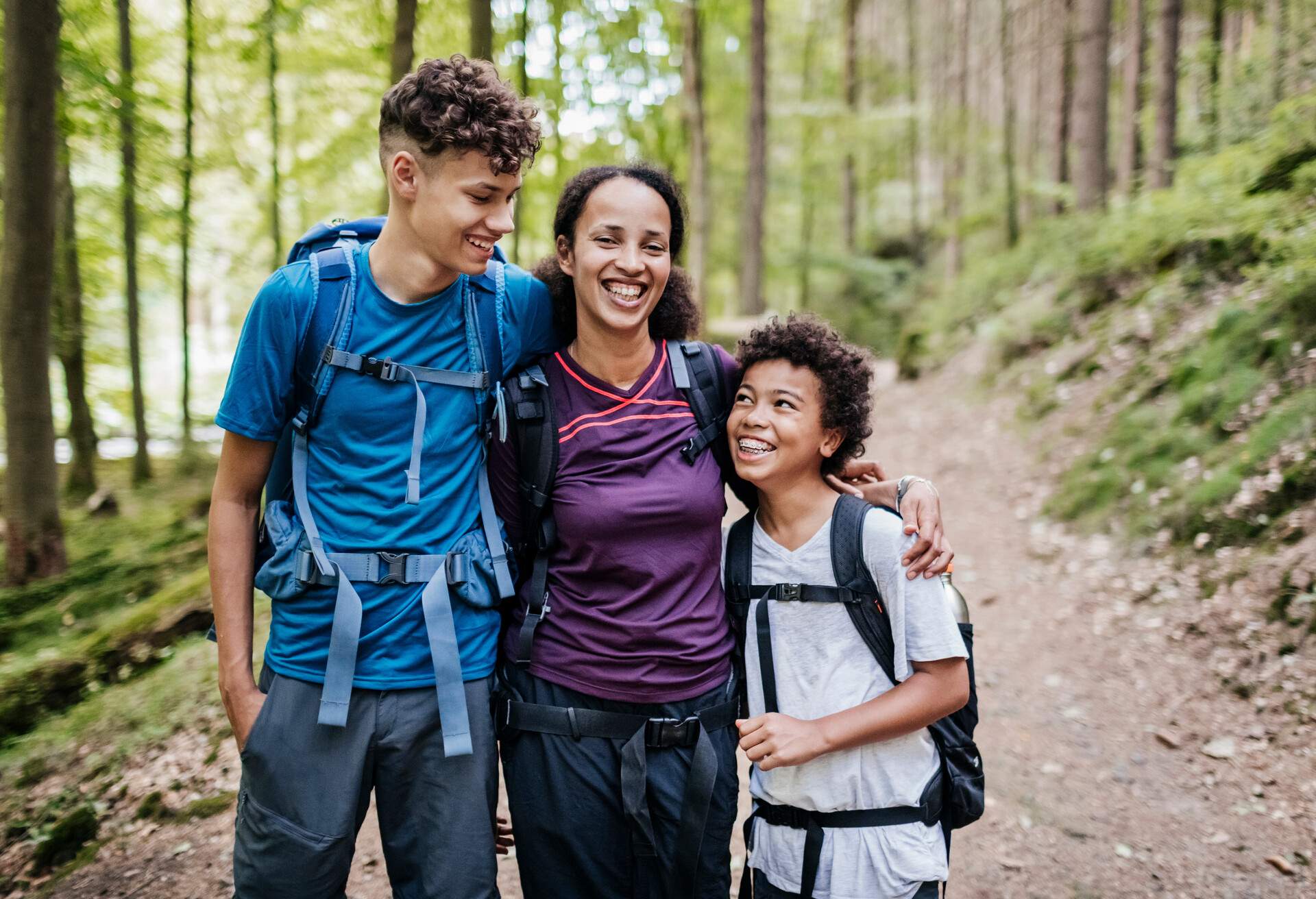 A family of three hugging while out hiking a woodland trail together.