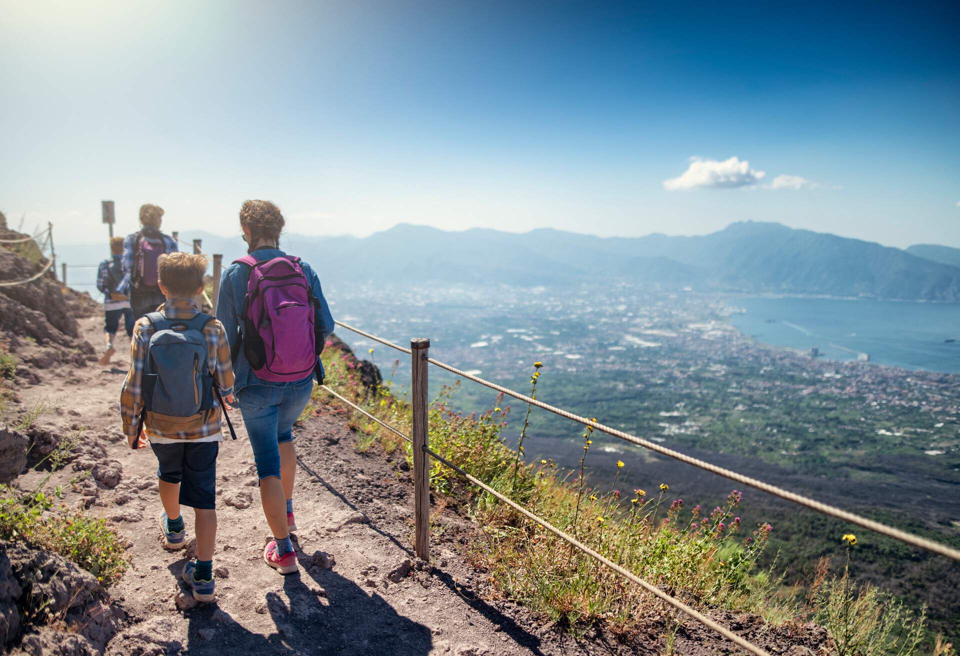 Family walking on the summit of Mount Vesuvius volcano in Campania, Italy. View of the gulf of Naples and the Lattari Mountains...Sunny summer day...Nikon D850
