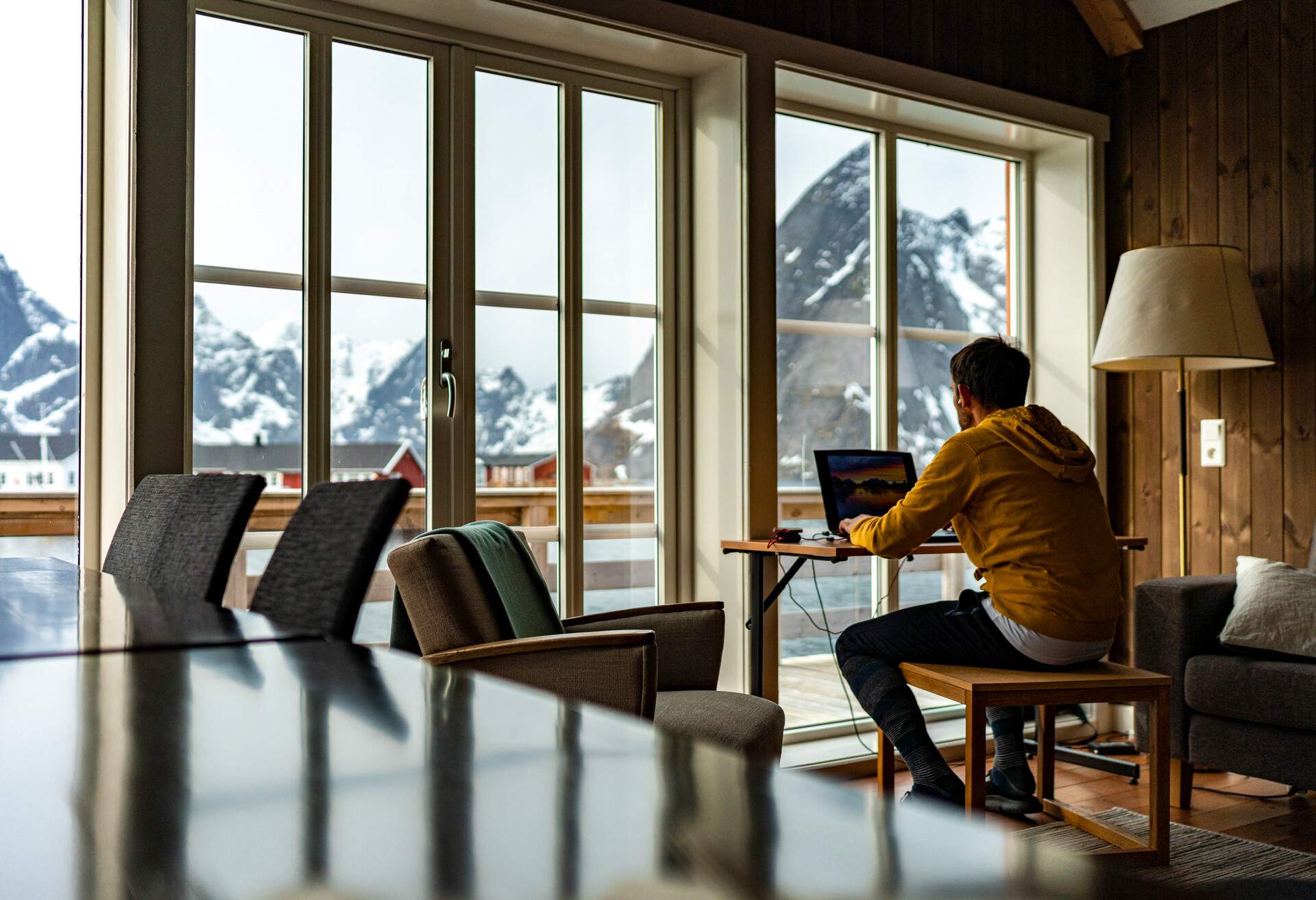 Person looking at mountains and sea from windows of traditional wood house while working with laptop, Lofoten islands, Norway