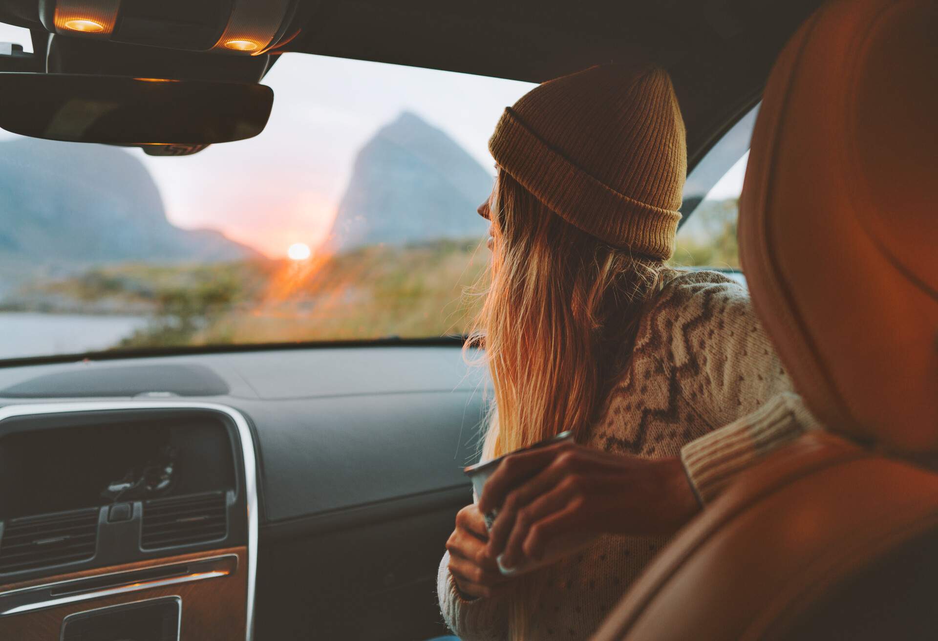 Woman on road trip traveling by rental car relaxing with coffee cup adventure lifestyle vacations vibes outdoor sunset Norway mountains view in window