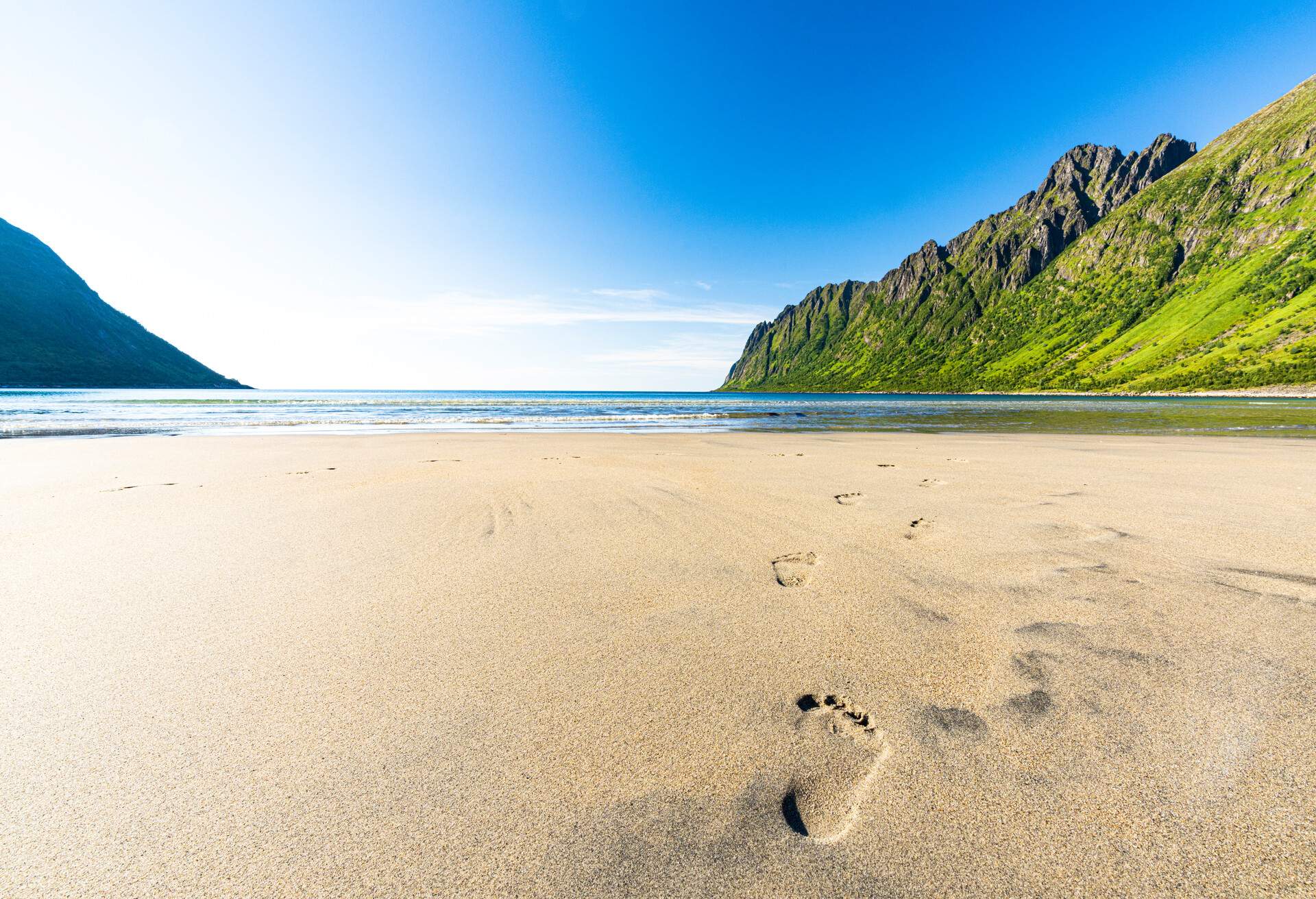 Sun shining over Ersfjord beach and fjord during summer with footprints in the sand, Senja, Troms county, Norway